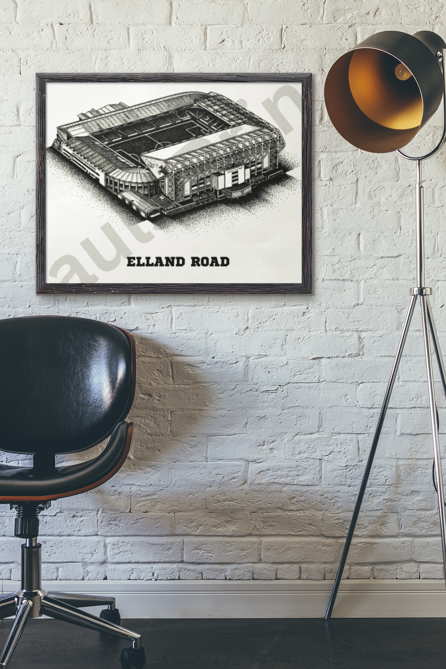 Framed football stadium artwork of Elland Road, mounted on white brick wall beside modern black chair and industrial standing lamp