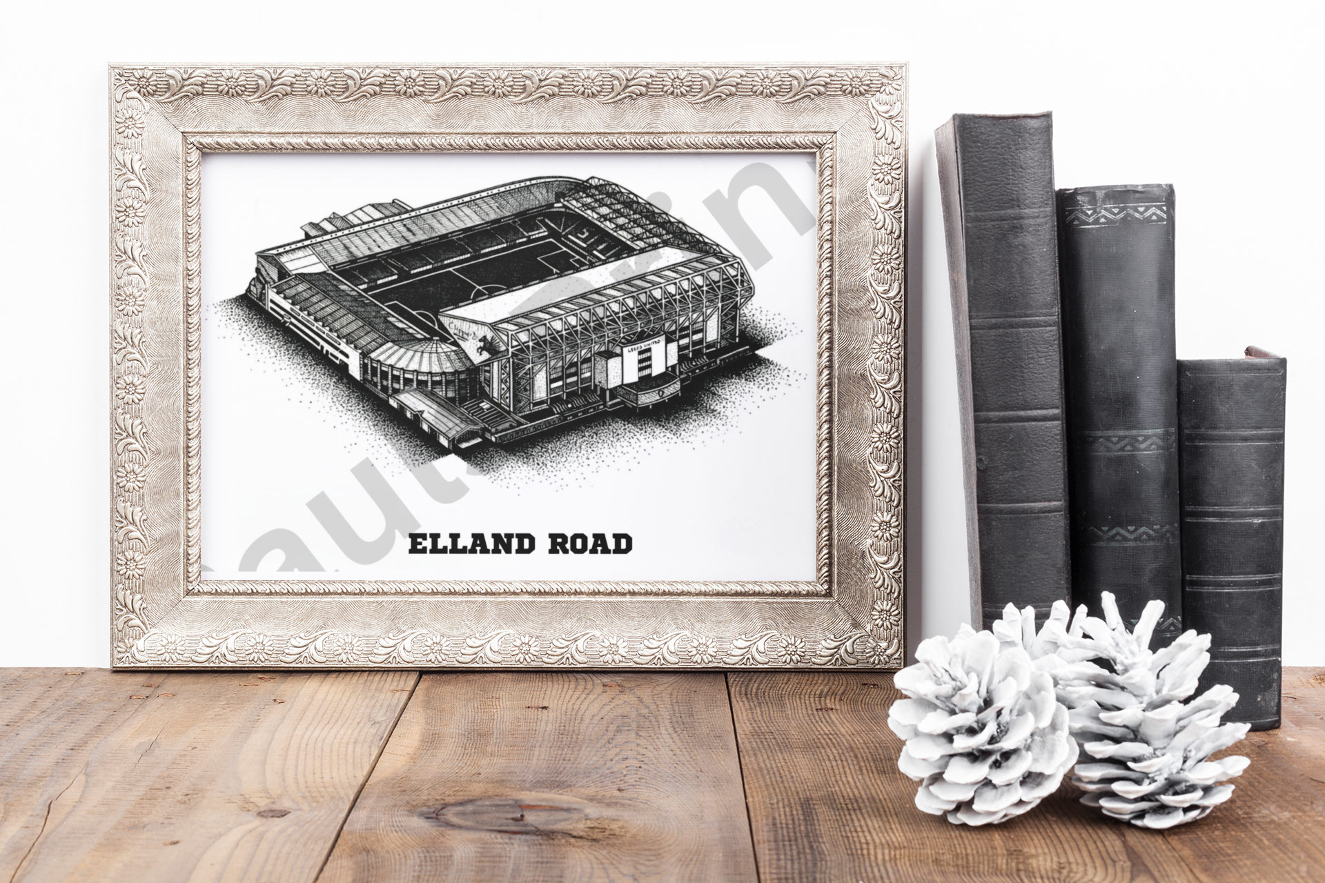 Framed Elland Road stadium print in ornate carved frame on wooden table with black books and white pinecones, ideal gift for Leeds fans