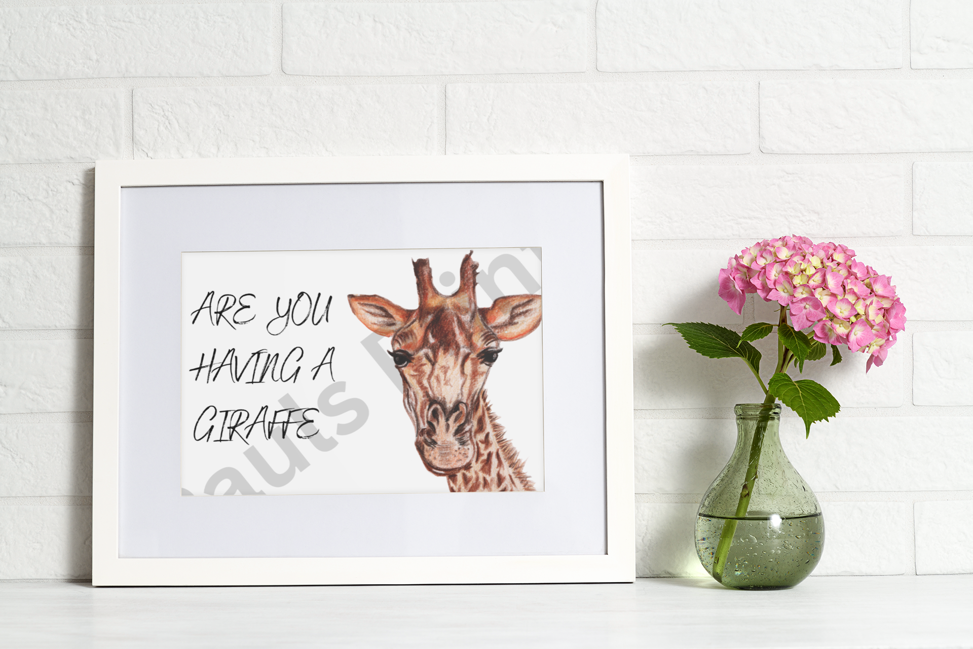 White framed giraffe print on a white brick wall, styled with a glass vase and pink flowers.