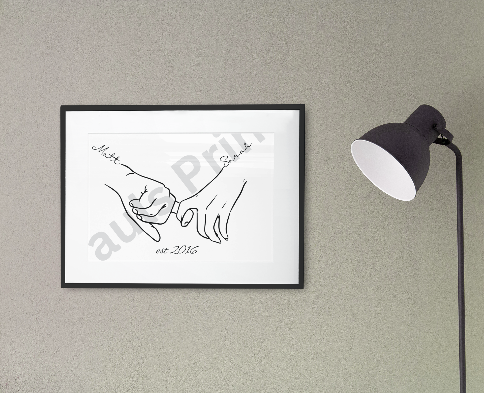 Personalised couple art print with names Matt and Sarah and est. 2016 text, framed in black and displayed on a grey wall beside a floor lamp
