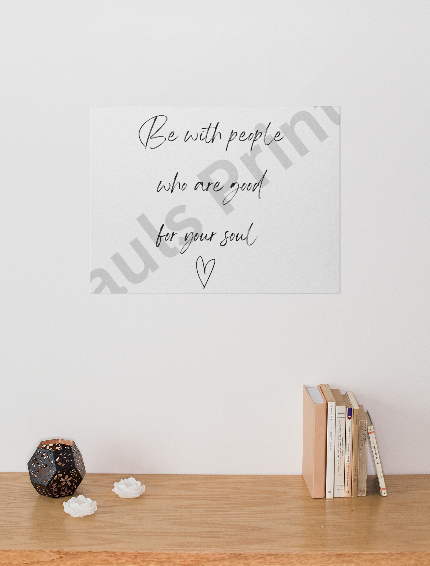 Typography print reading “Be with people who are good for your soul” above a wooden console with books, a black candle holder, and white flower ornaments.