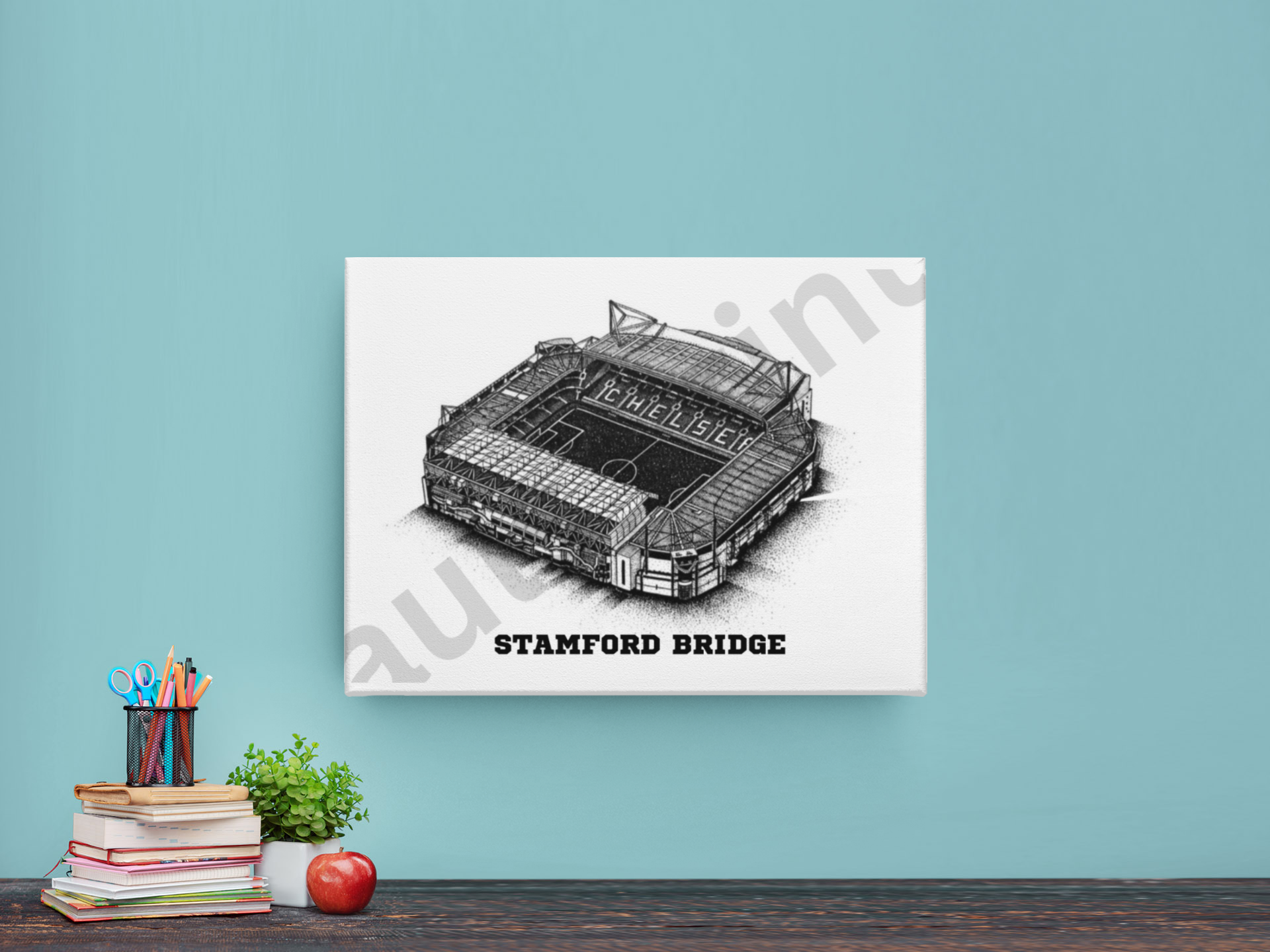 Stamford Bridge stadium artwork printed on canvas, displayed on a blue wall above a desk with books, plant, and stationery.