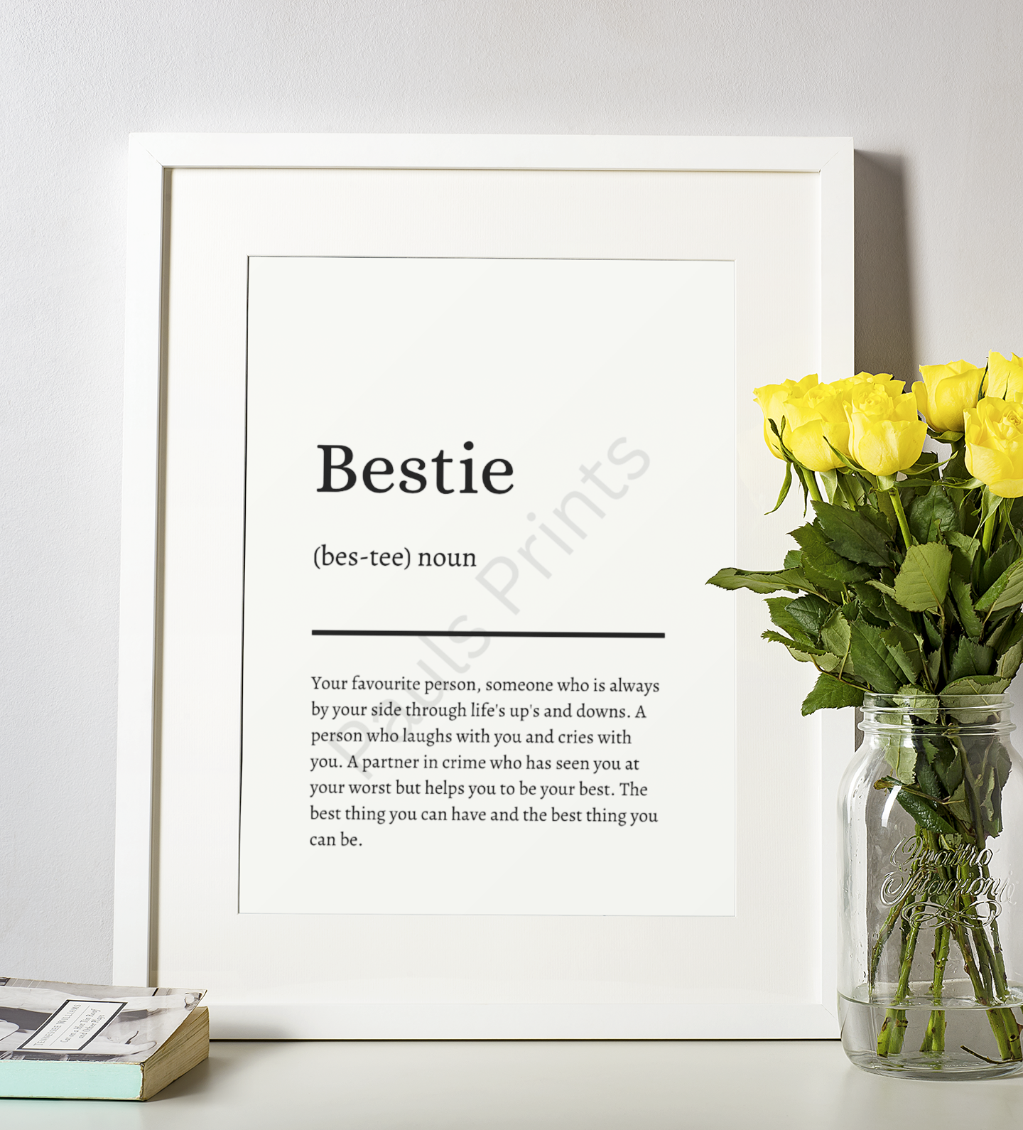 White-framed "Bestie" definition print displayed beside a bouquet of yellow roses in a glass jar vase.
