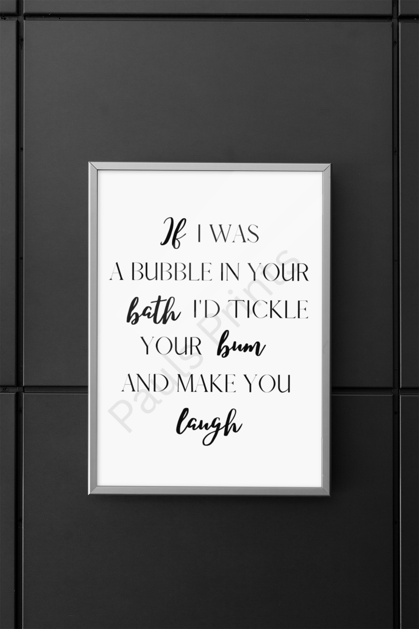 White-framed humorous bathroom print with playful quote, hung on a dark black-tiled wall.