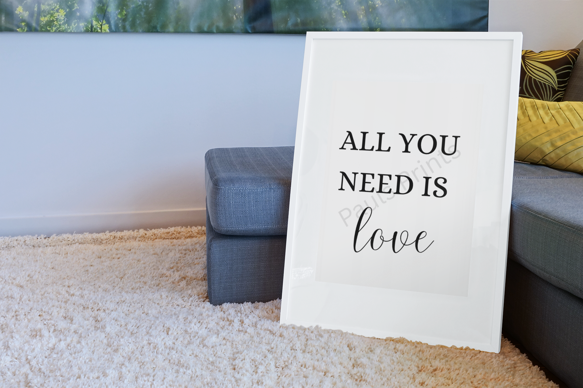 White-framed print with the words "All you need is love," placed on a cream shaggy rug beside a grey sofa with yellow cushions.