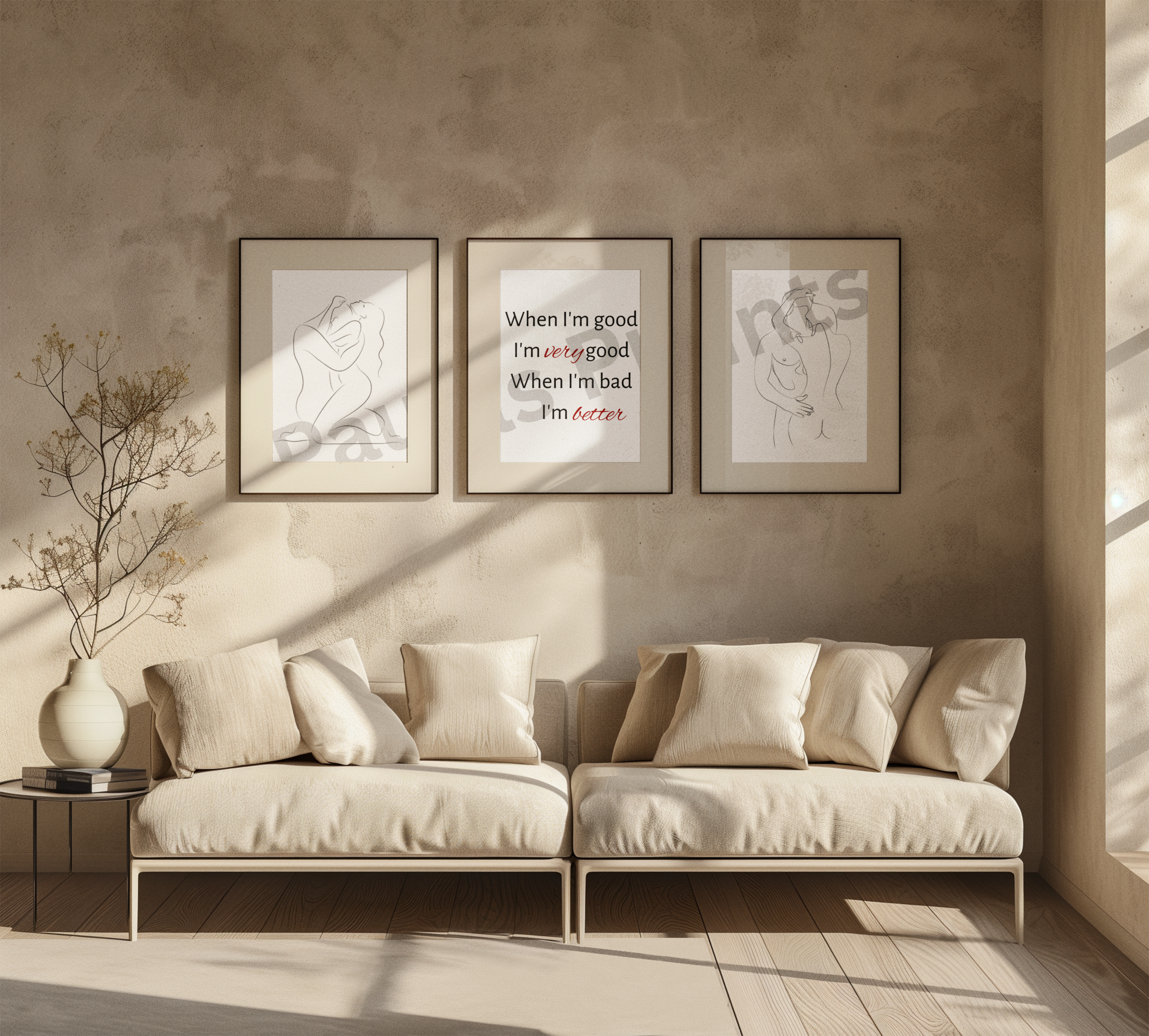 A warm, minimalist living room featuring two beige sofas with cream cushions, a round side table with a vase and books, and three framed wall art pieces above the sofa. The center artwork displays the quote: "When I'm good I'm very good, When I'm bad I'm better." Sunlight streams in through large windows, casting soft shadows on the textured beige wall.