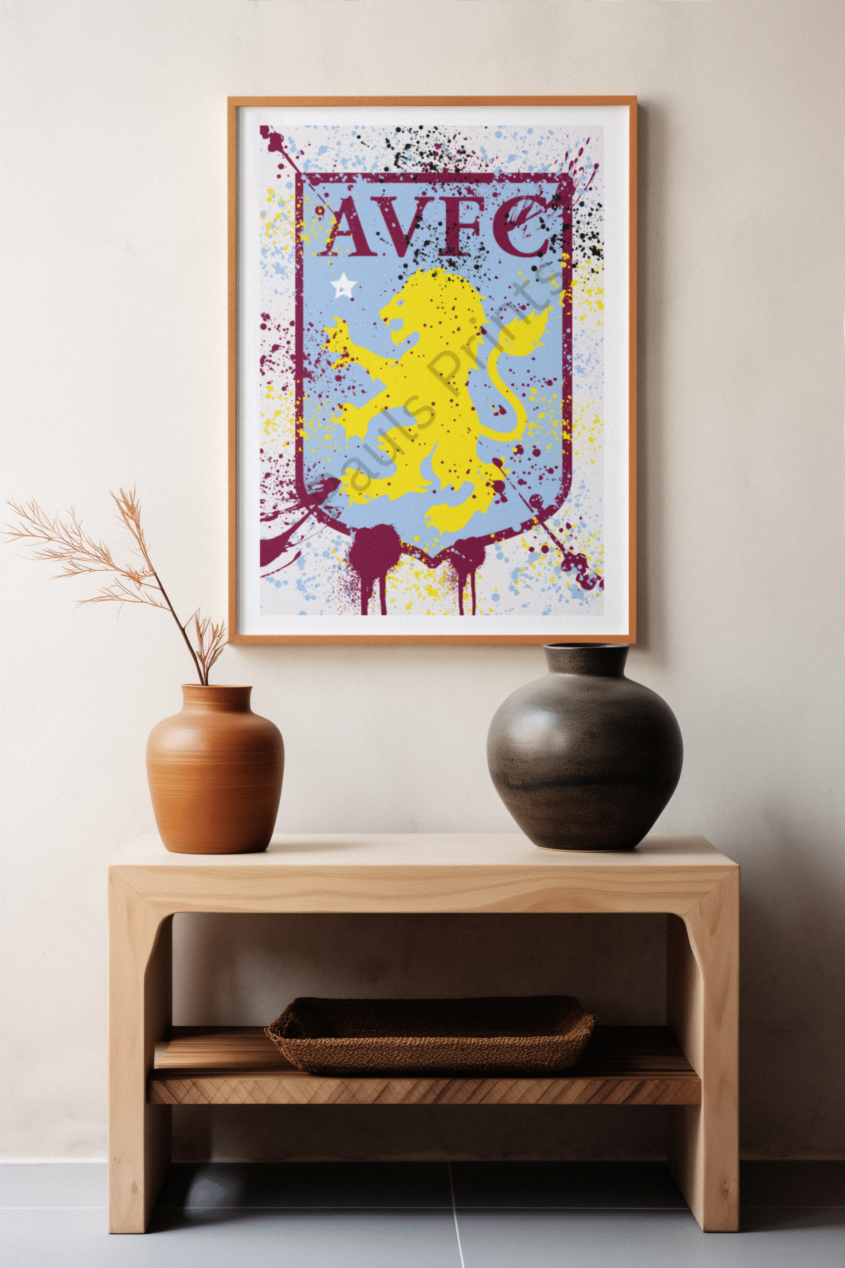 Contemporary Aston Villa FC crest artwork with vibrant splatter effects, framed in light wood and displayed above decorative vases.