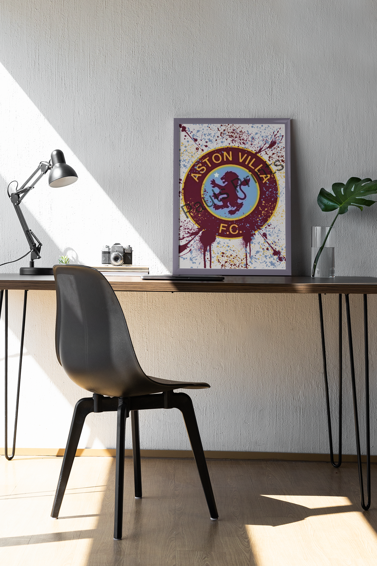 Aston Villa FC art leaning on desk in bright, modern home office with black chair and potted plant.