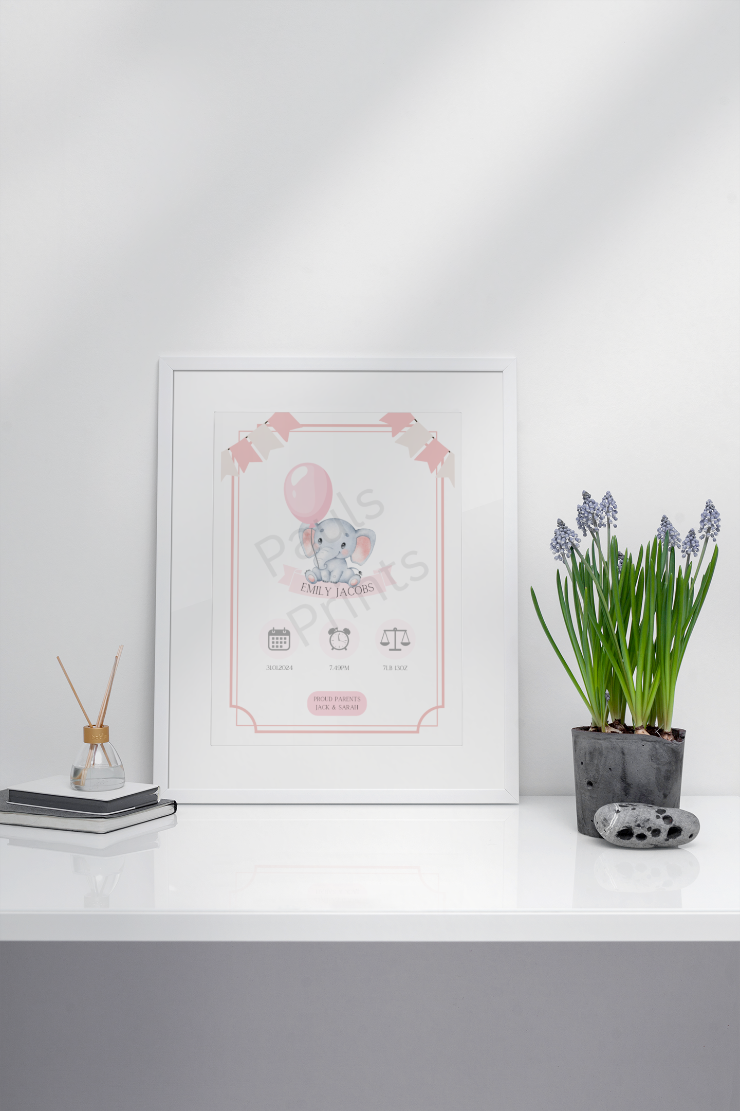 Customisable elephant baby print with soft pink bunting, framed and placed on a glossy white cabinet beside a flower pot.