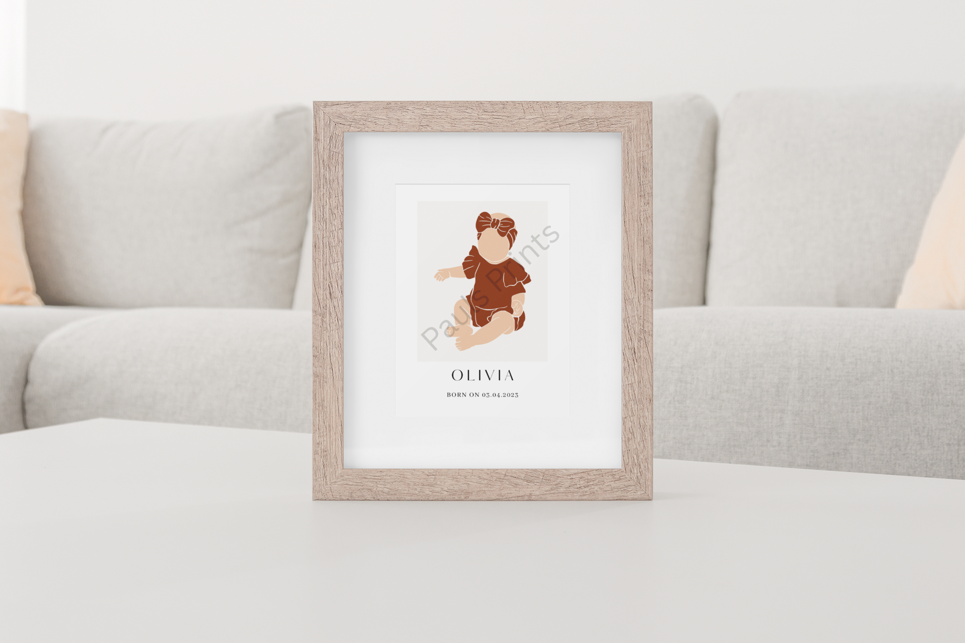 Neutral baby girl portrait in a wooden frame, displayed on a white coffee table in front of a beige sofa.