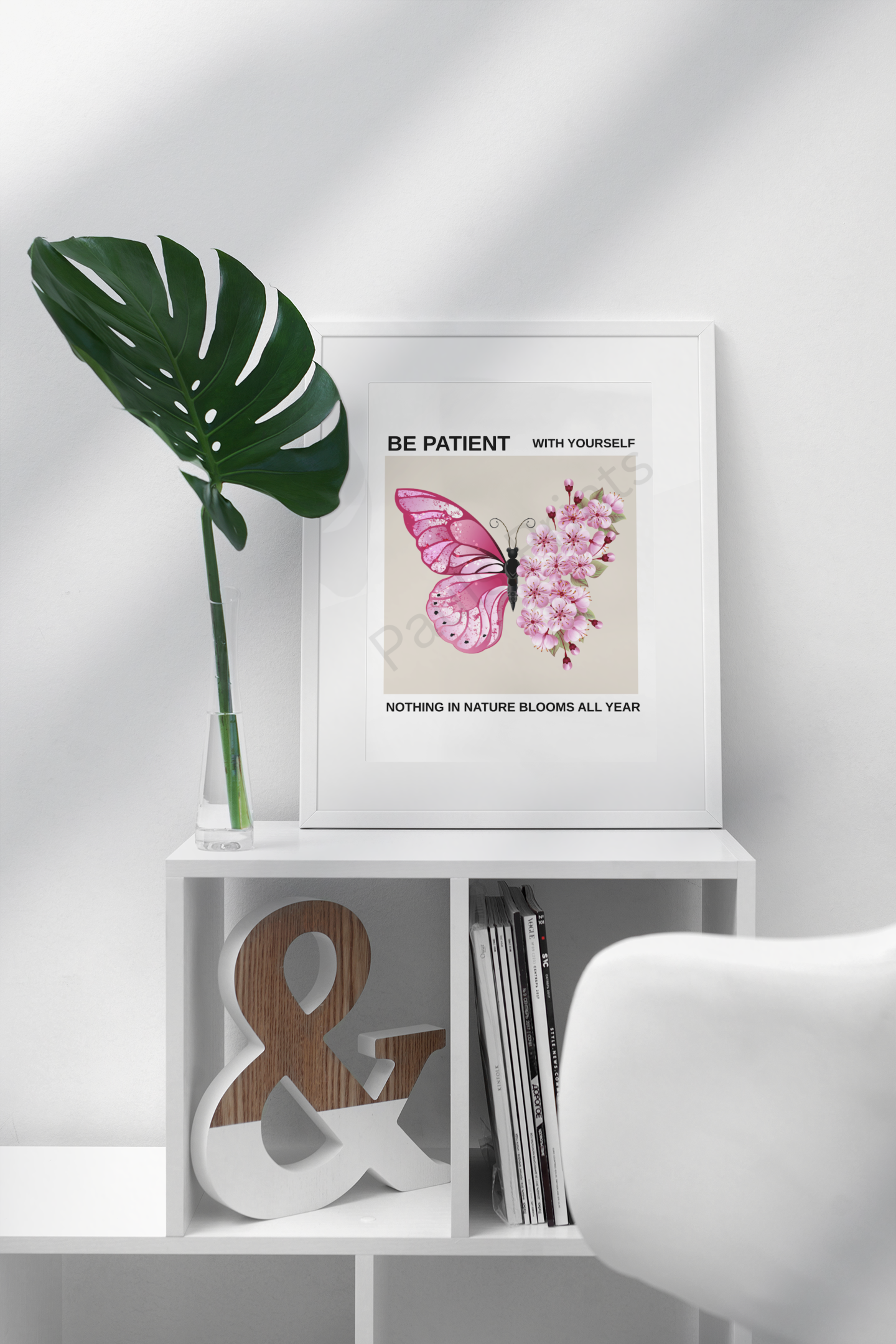 Framed pink butterfly and cherry blossom print with motivational quote "Be Patient With Yourself, Nothing In Nature Blooms All Year," displayed on white cube shelf beside a green leaf in vase.