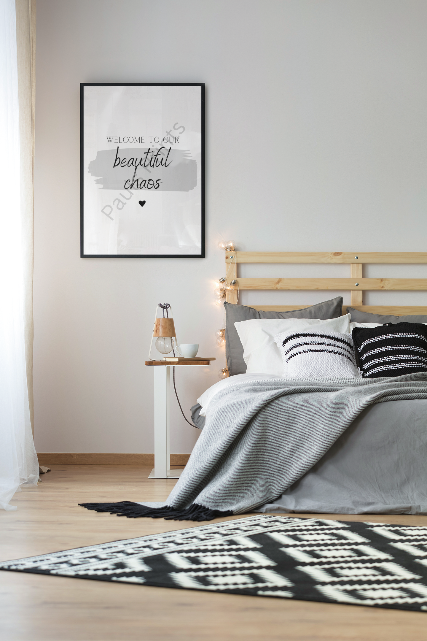 “Welcome to our beautiful chaos” print above bed with grey bedding, monochrome cushions, and Scandinavian bedside table.