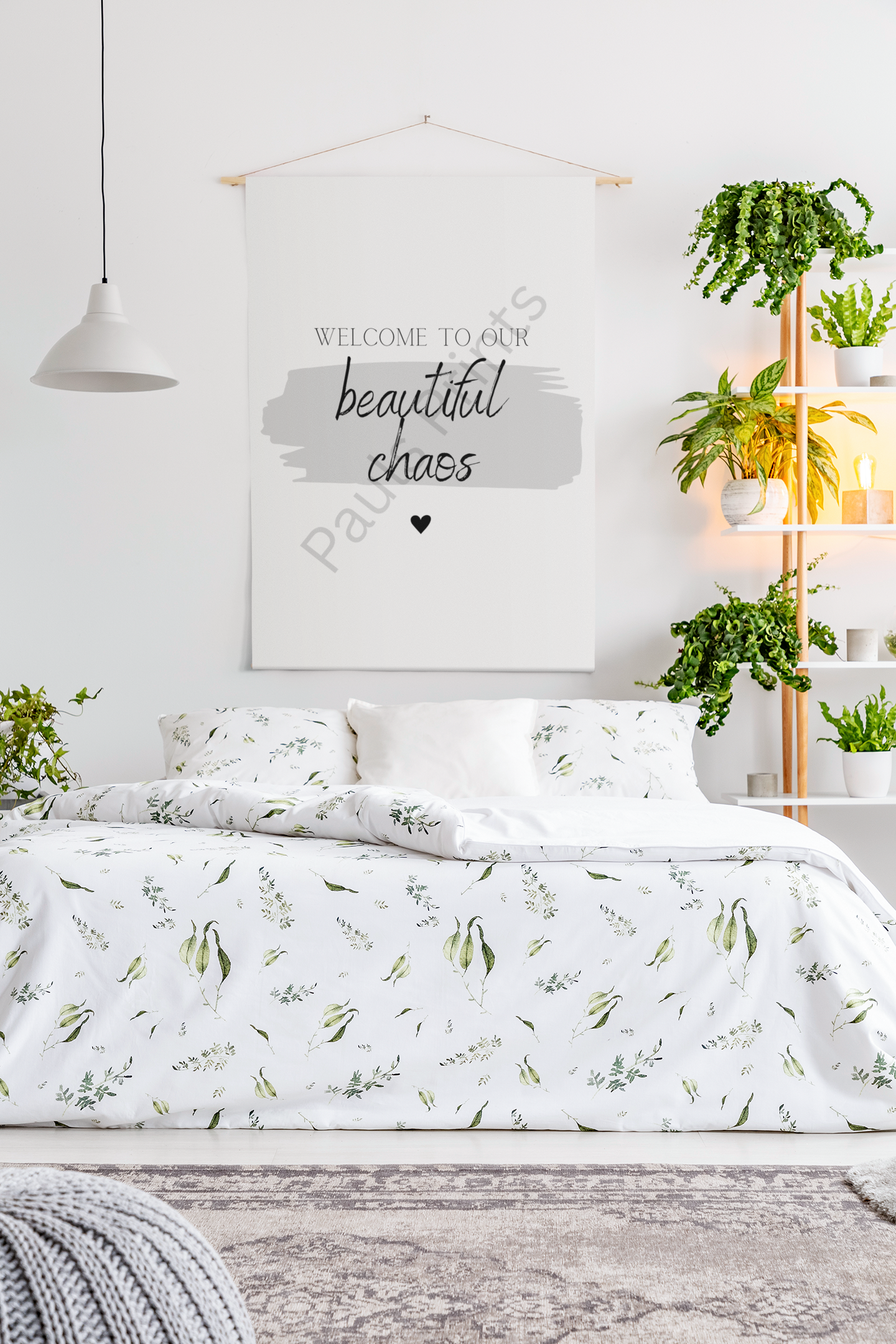 “Welcome to our beautiful chaos” canvas print in a white bedroom with leafy bedding and shelves filled with plants.