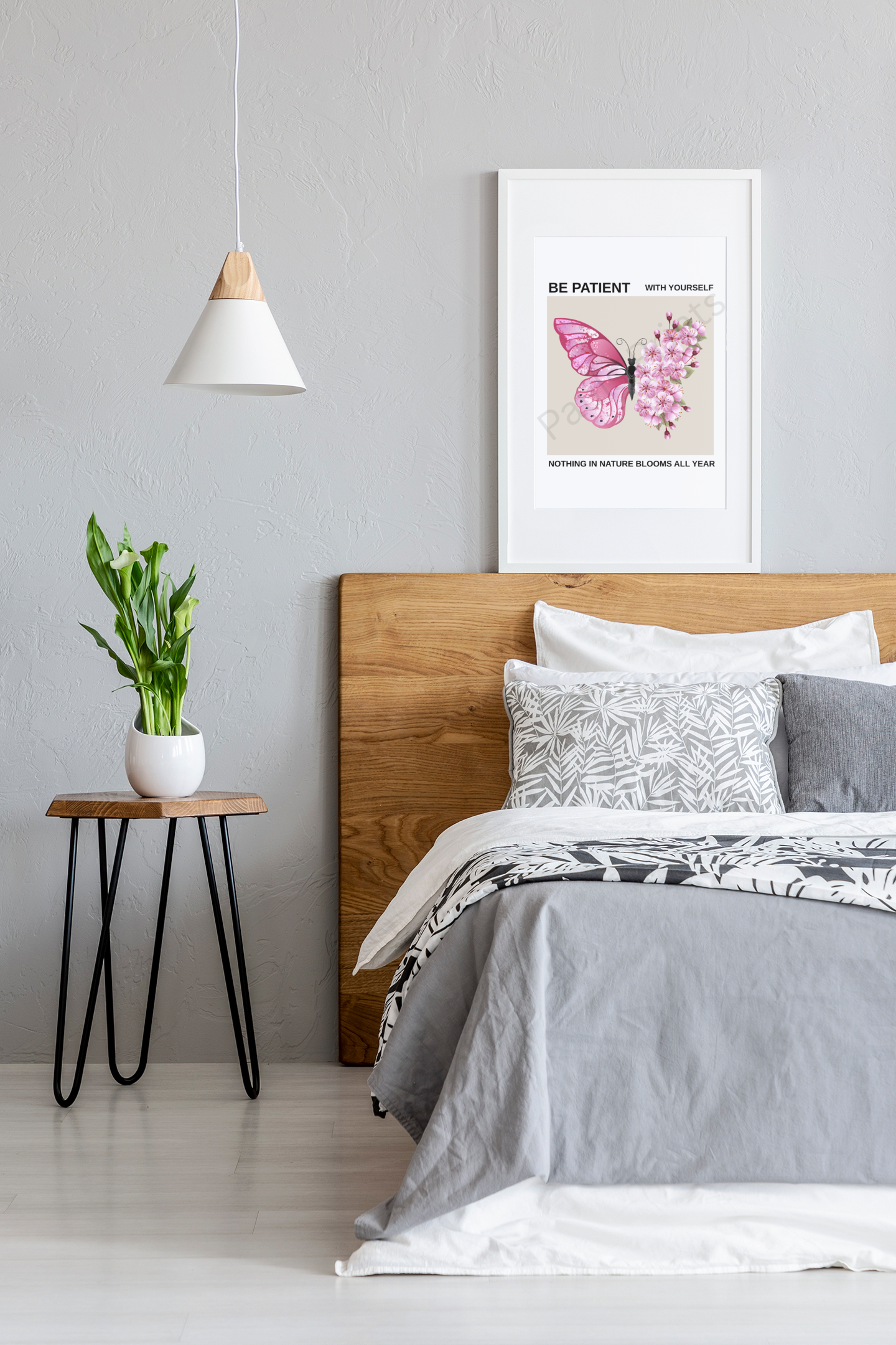 White-framed butterfly and cherry blossom motivational print hung above wooden bed headboard in modern bedroom with grey walls and white pendant light.