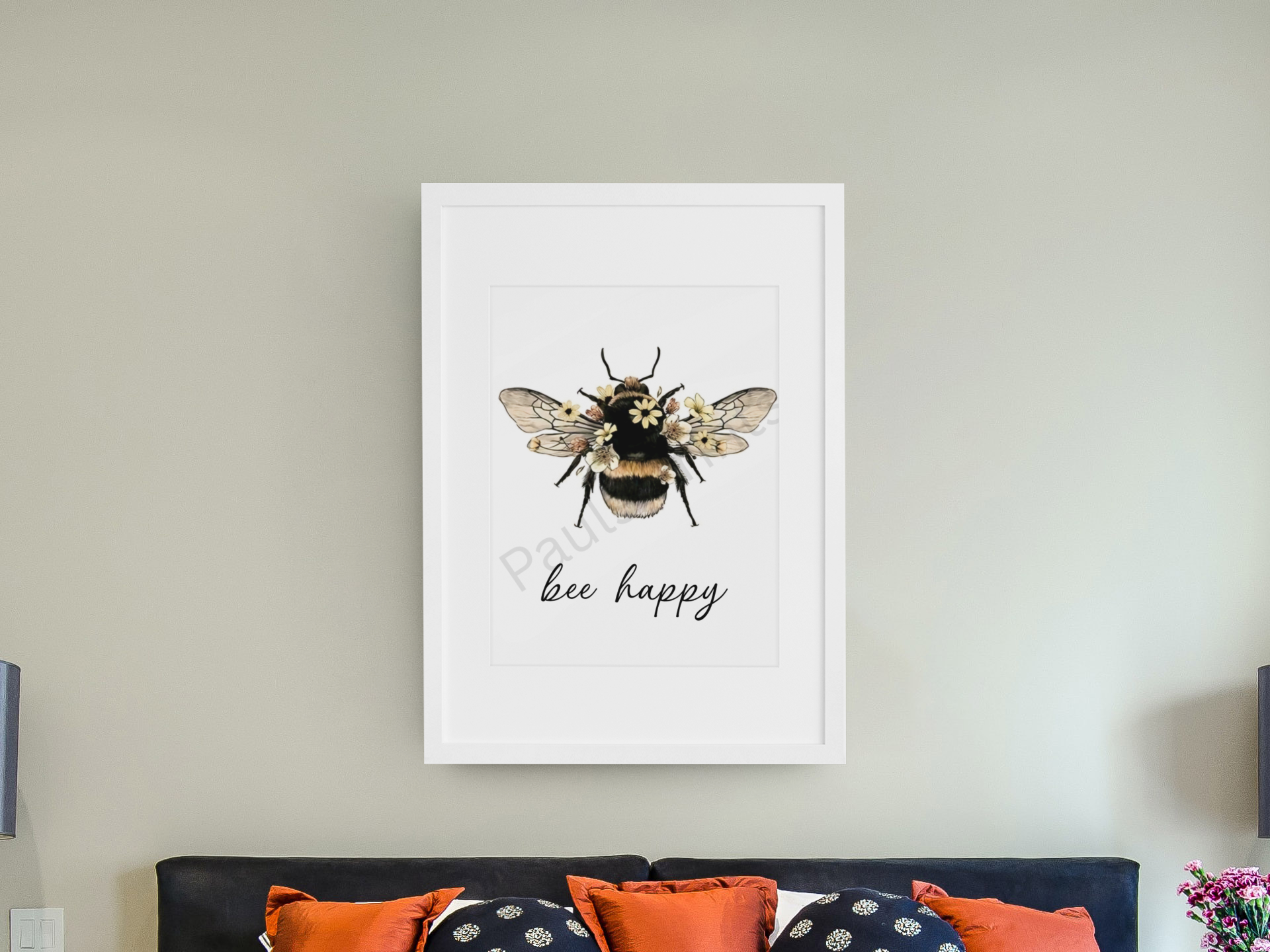 Elegant bee illustration with floral accents and “bee happy” quote, framed in white and displayed above a bed with orange and navy pillows.