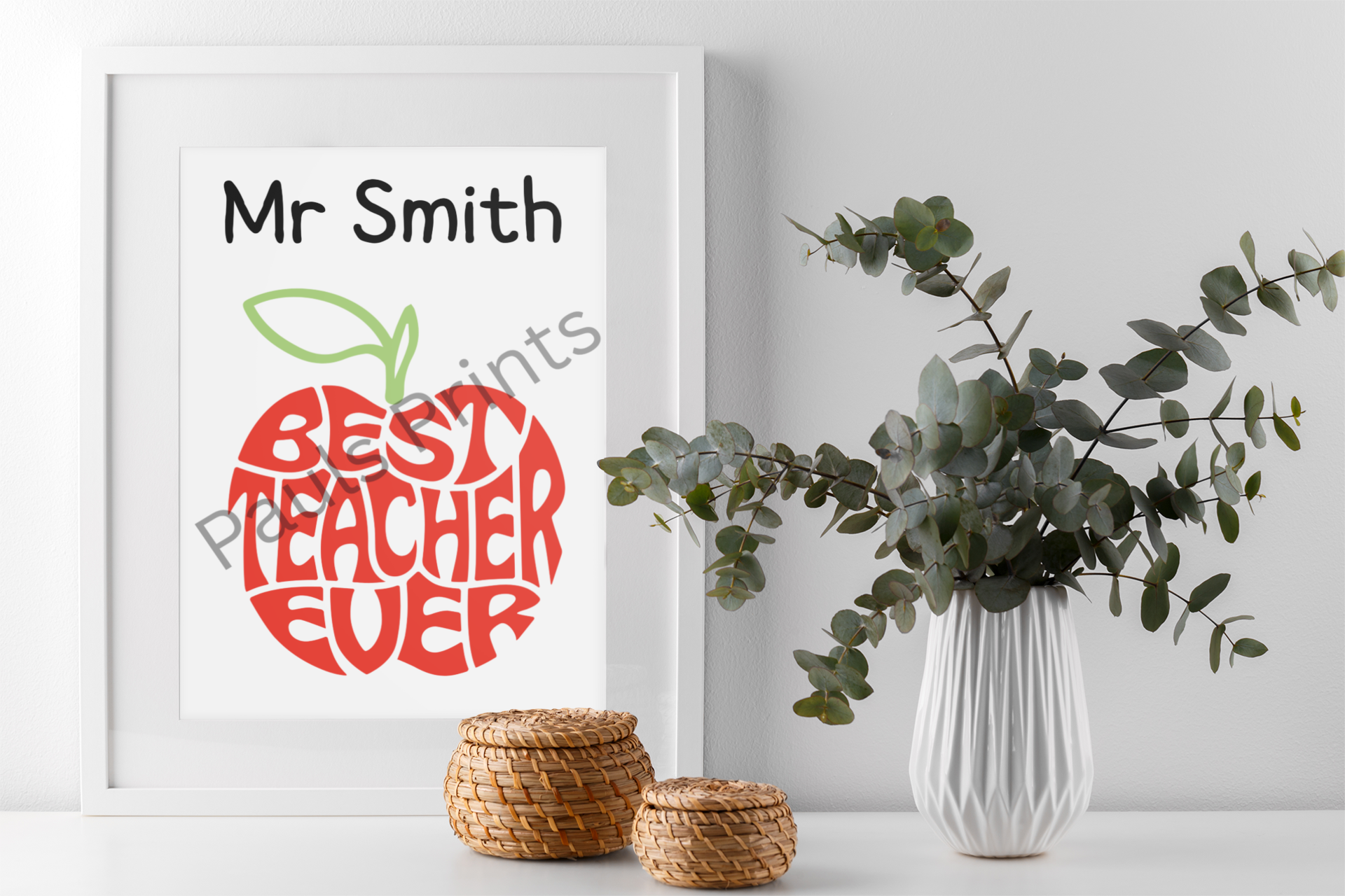 Personalised Best Teacher Ever framed print on white wall beside wicker baskets and a vase with eucalyptus branches.