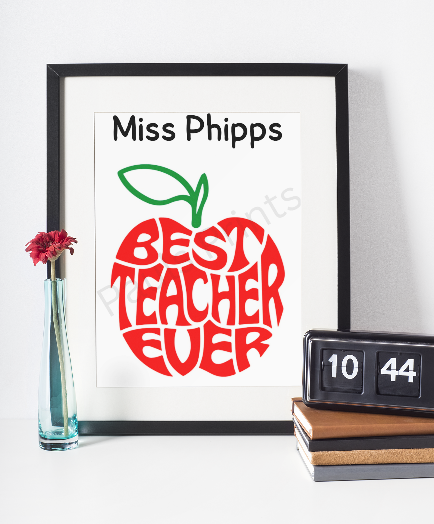 Black-framed “Best Teacher Ever” apple print with teacher’s name, styled with a red flower in a vase and retro flip clock.