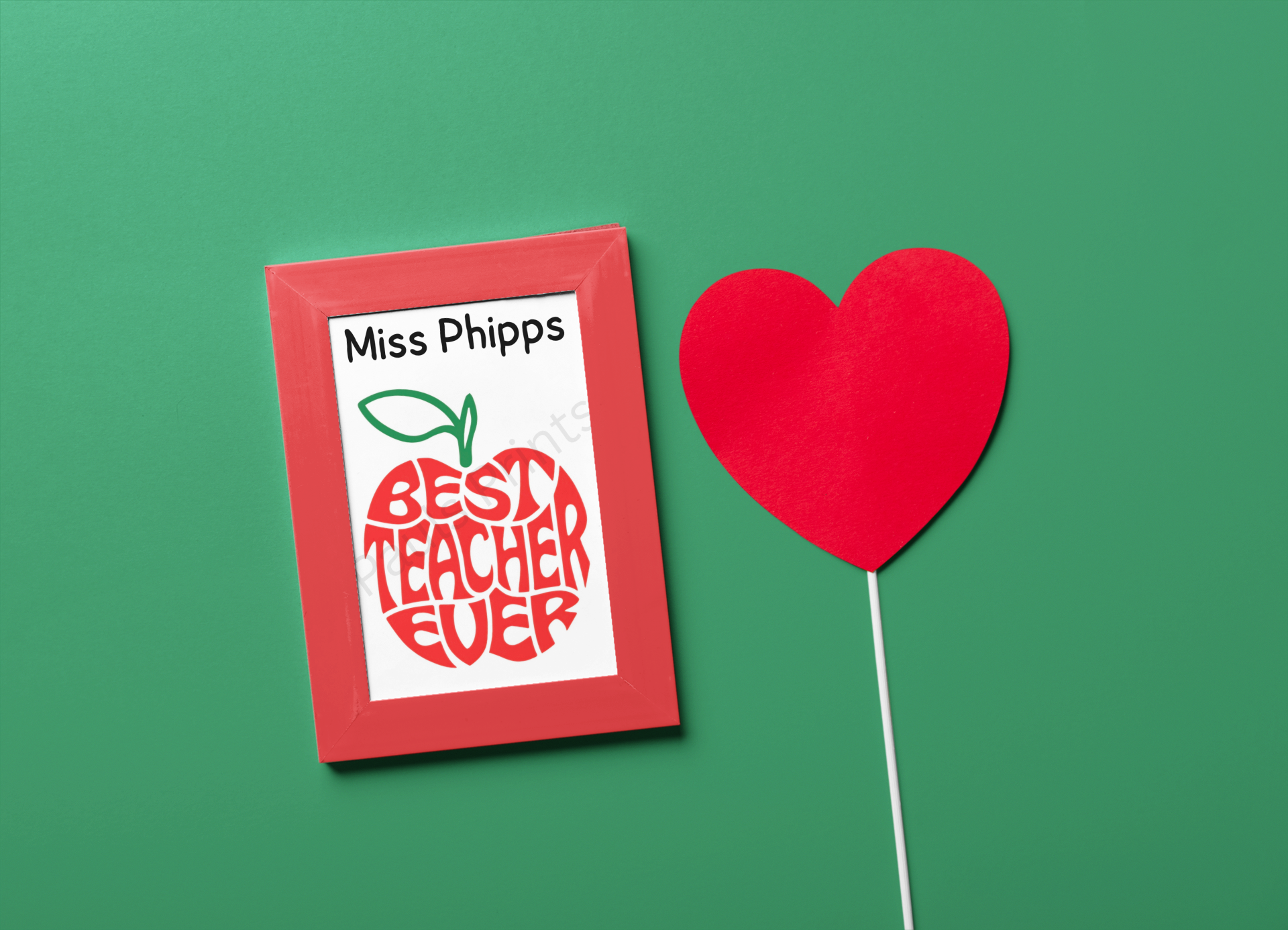 Framed “Best Teacher Ever” print with red apple design and teacher’s name, displayed against a green background with heart decoration.