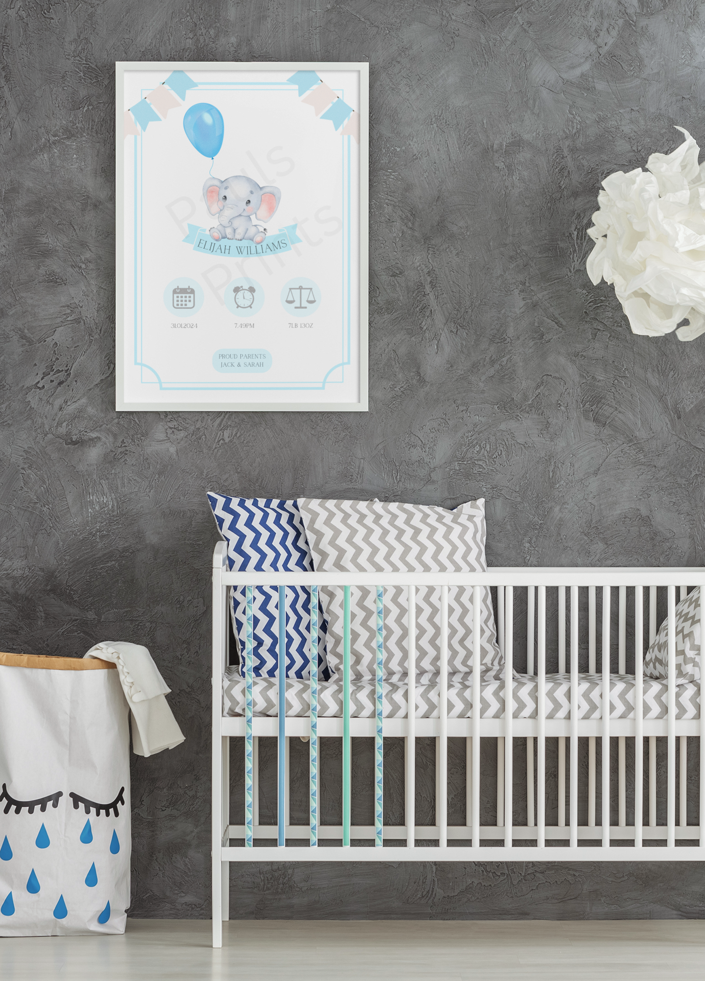 Elephant-themed baby print with blue accents, hung above a cot with chevron cushions against a grey textured wall.
