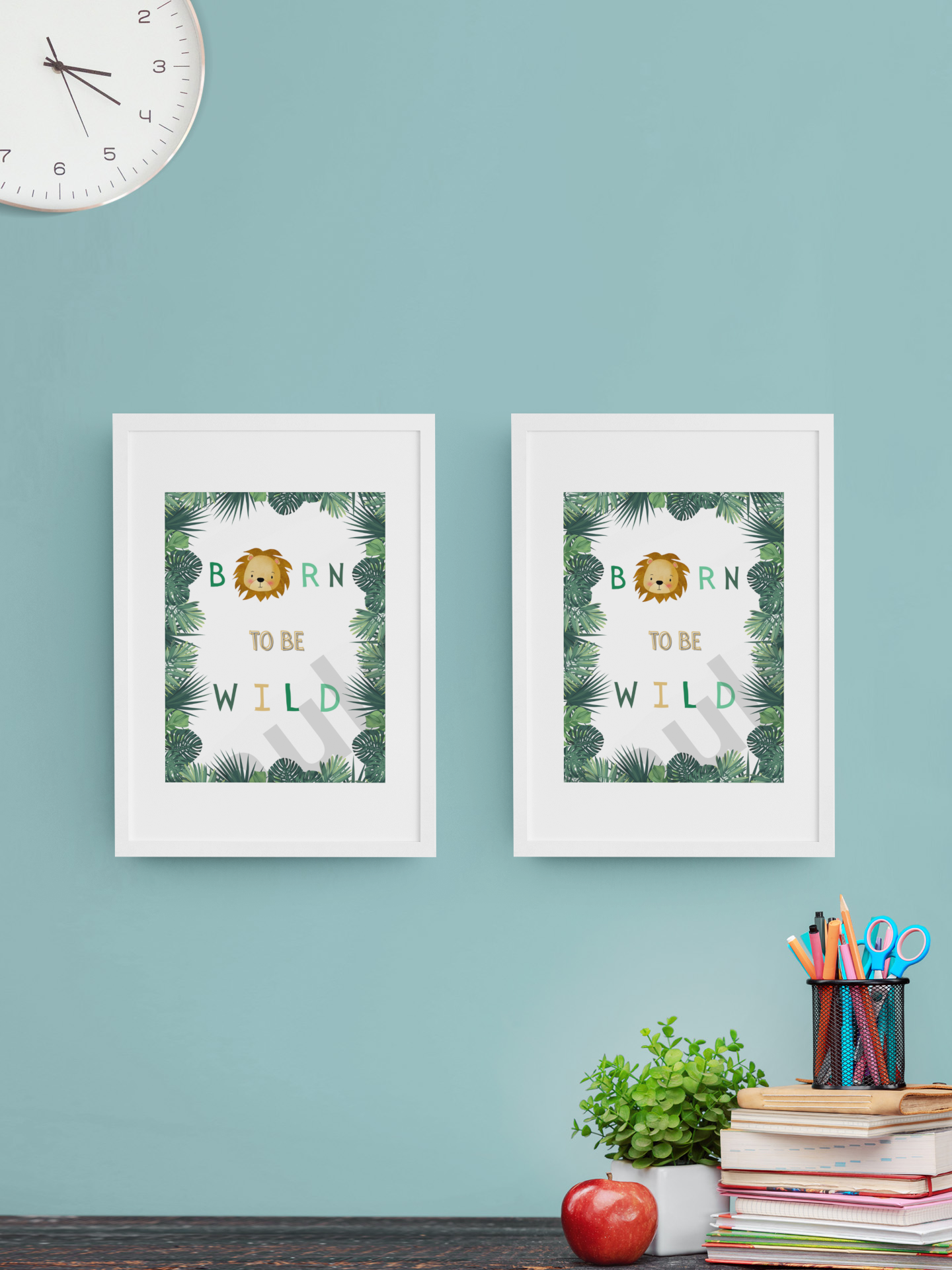 A playful study space featuring twin jungle-themed prints—one with the phrase “Born to be Wild” and the other with a lion illustration—framed in white against a pastel teal wall, with school supplies and books adding charm.