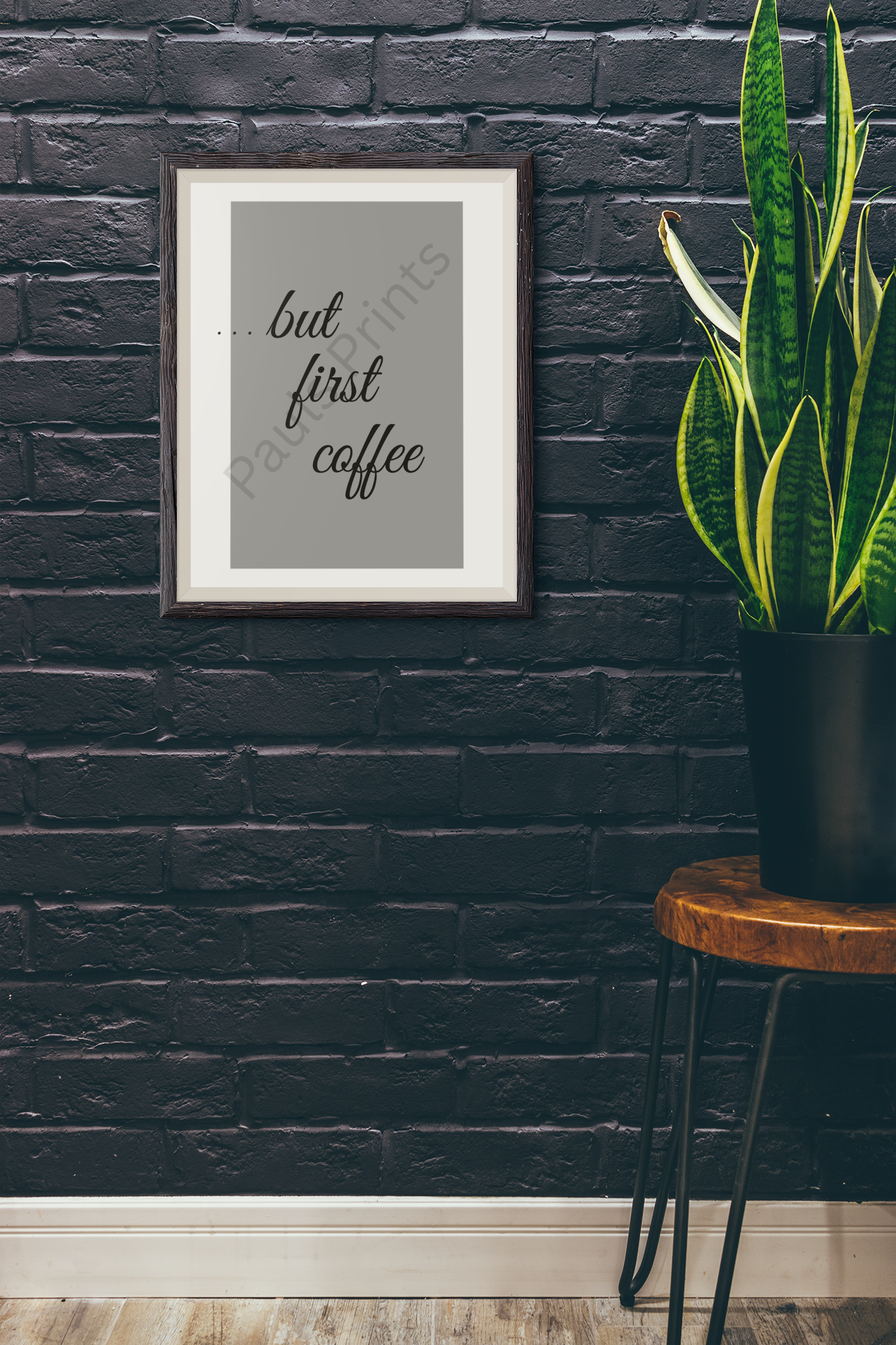 Coffee quote framed print mounted on a dark exposed brick wall beside a snake plant and rustic table.