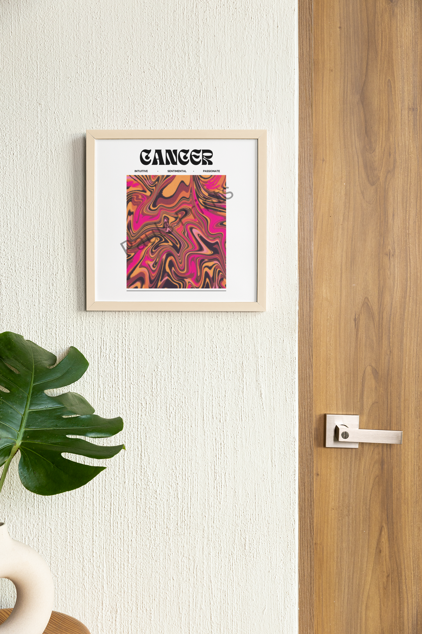 Framed Cancer zodiac artwork in pink tones, hanging beside a wooden door and potted monstera plant, giving a warm and tropical touch to the space.