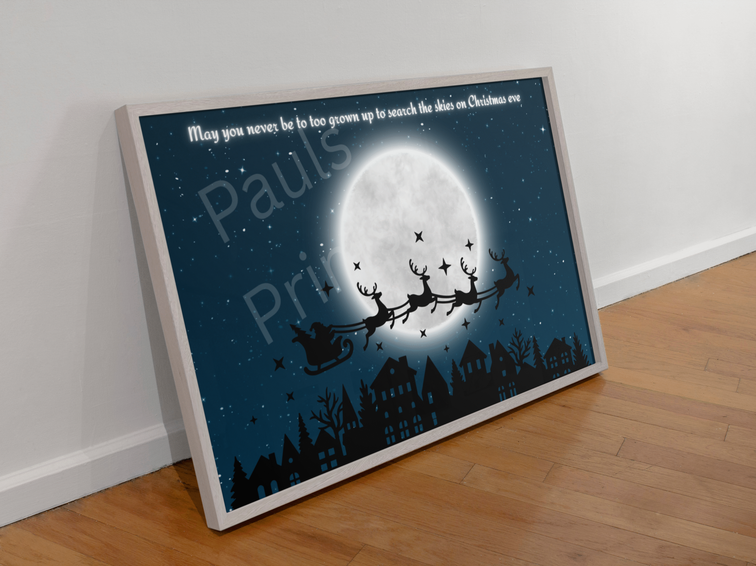 Wooden-framed Christmas Eve Santa sleigh print leaning against a white wall on a wooden floor.