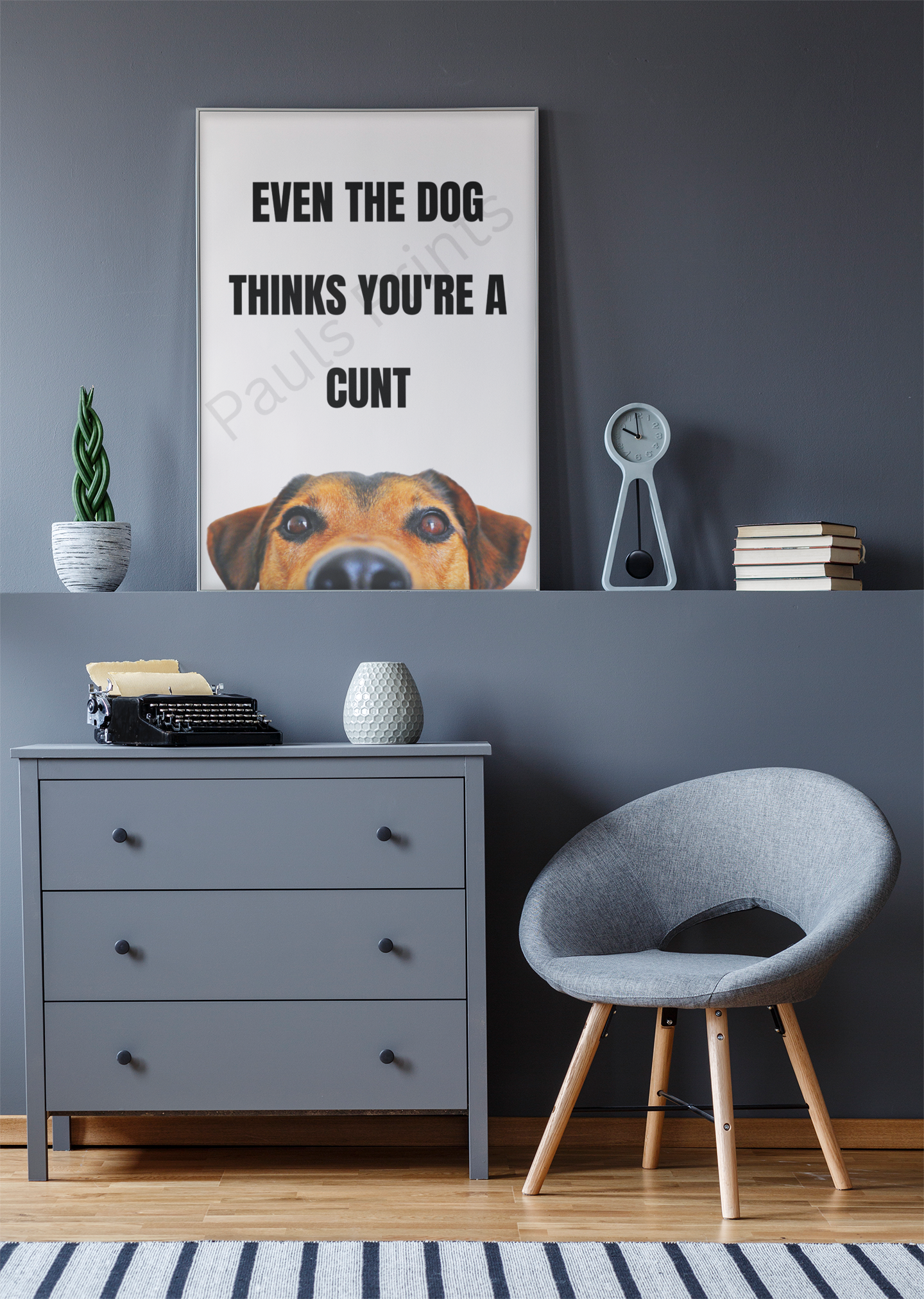 Humorous framed dog quote print with black text and peeking dog graphic, styled against a grey wall with matching grey furniture and decorative accessories.
