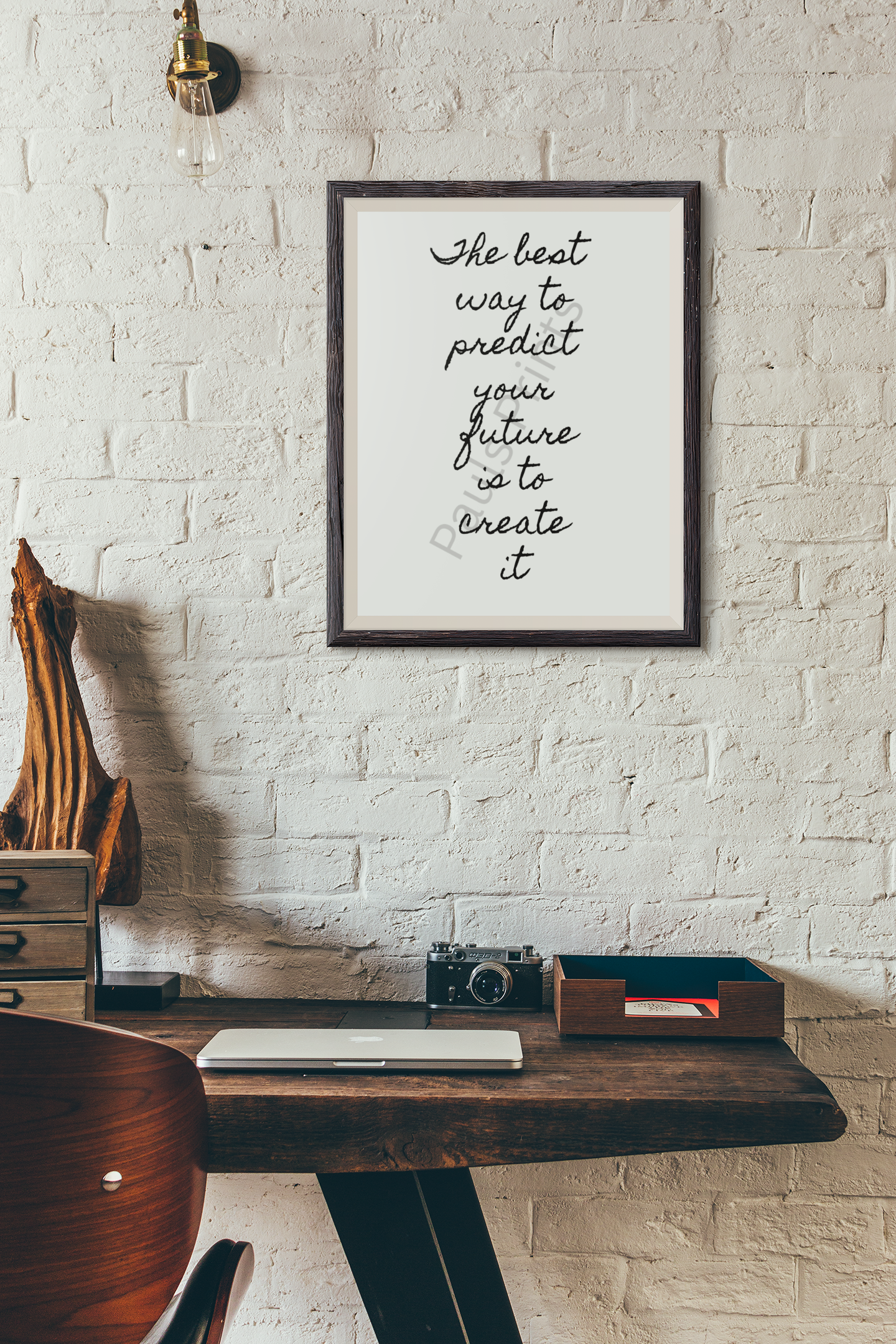 Framed motivational print on exposed white brick wall above a wooden desk with vintage camera, lamp and natural textures.