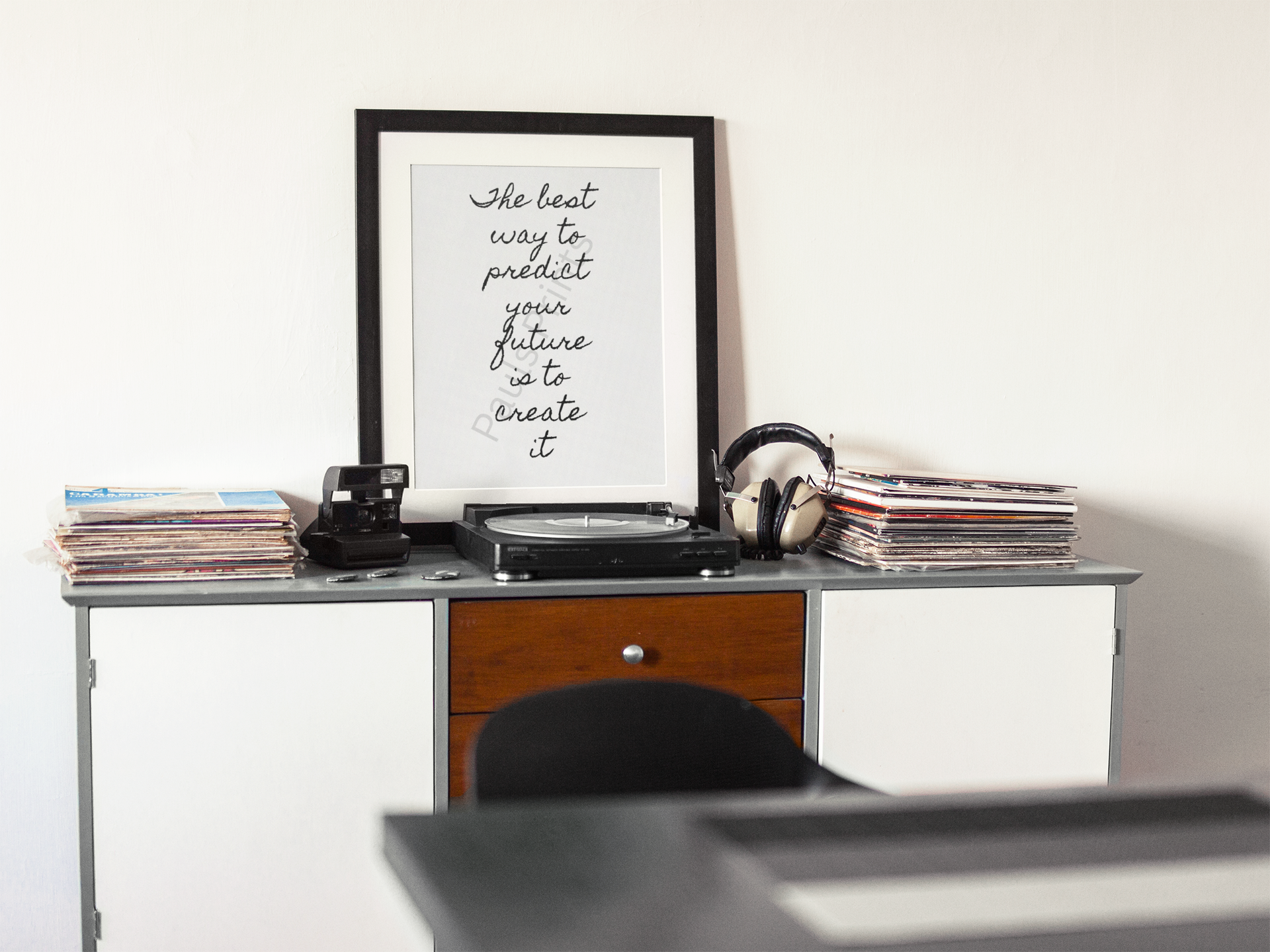 Black framed inspirational print surrounded by vinyl records, a record player, and headphones in a retro music room.