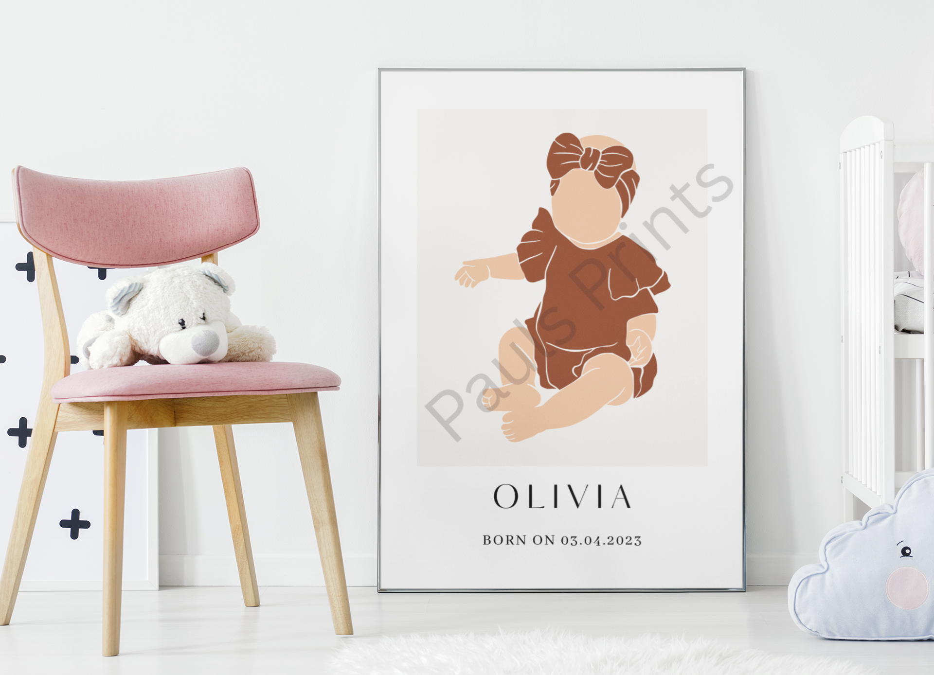 Framed personalised baby print with brown outfit, styled next to a pink chair and soft teddy bear in a nursery.