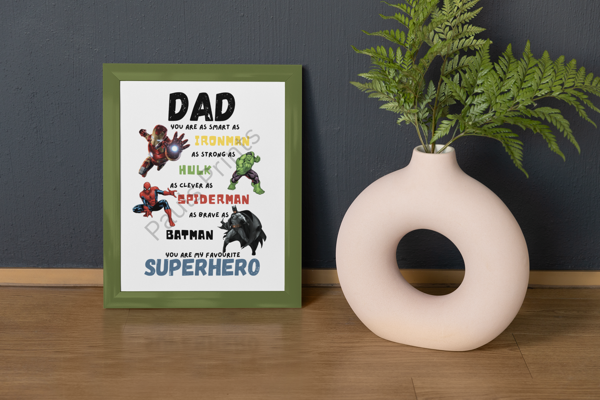 Colourful superhero-themed dad print in a green frame, styled against a dark wall beside a modern vase and fern.