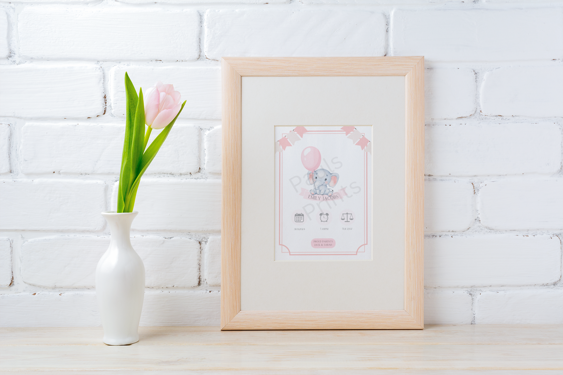 Pastel pink elephant baby print in a wooden frame, styled on a rustic shelf with tulip vase and white brick background.