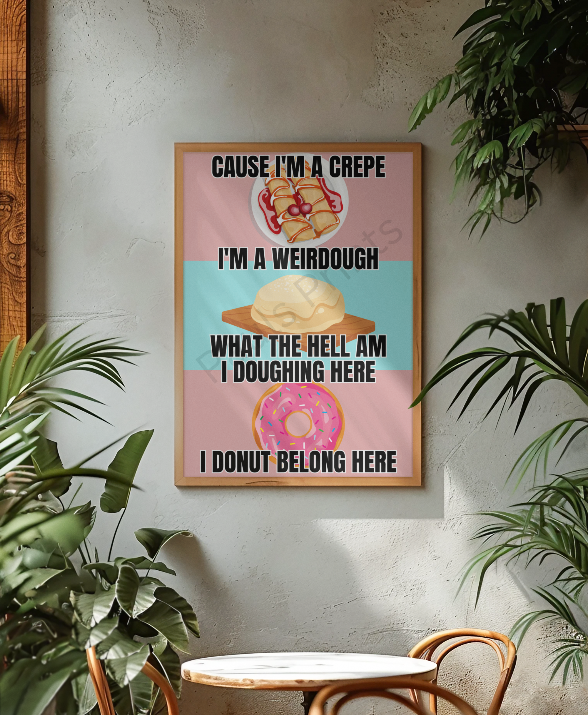 Humorous wall art with illustrations of a crepe, dough ball, and donut, featuring playful baking puns in bold black text. Displayed in a wooden frame on a textured wall surrounded by green plants