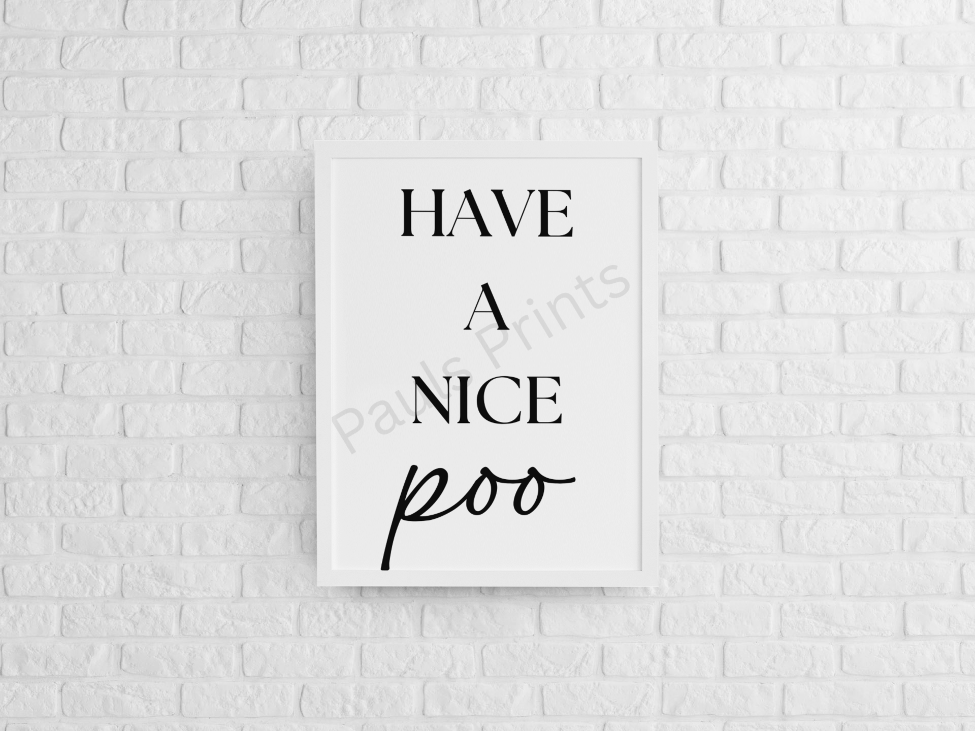 Humorous black and white framed bathroom wall art print with the text “Have a Nice Poo” on a white brick wall.