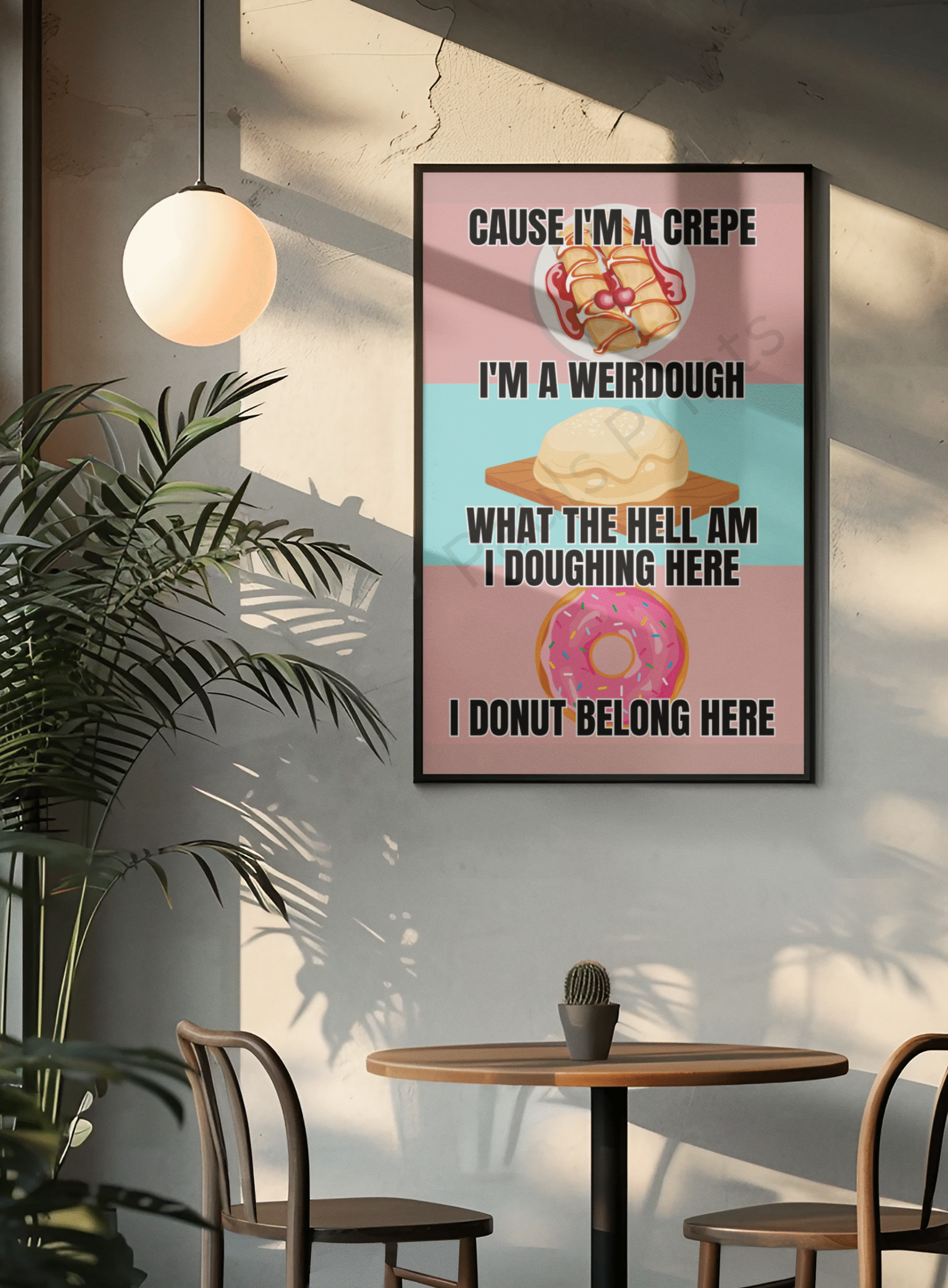 Whimsical baking pun wall print with crepe, dough, and donut illustrations, framed in black and hanging in a cozy cafe-style corner with a small round table.