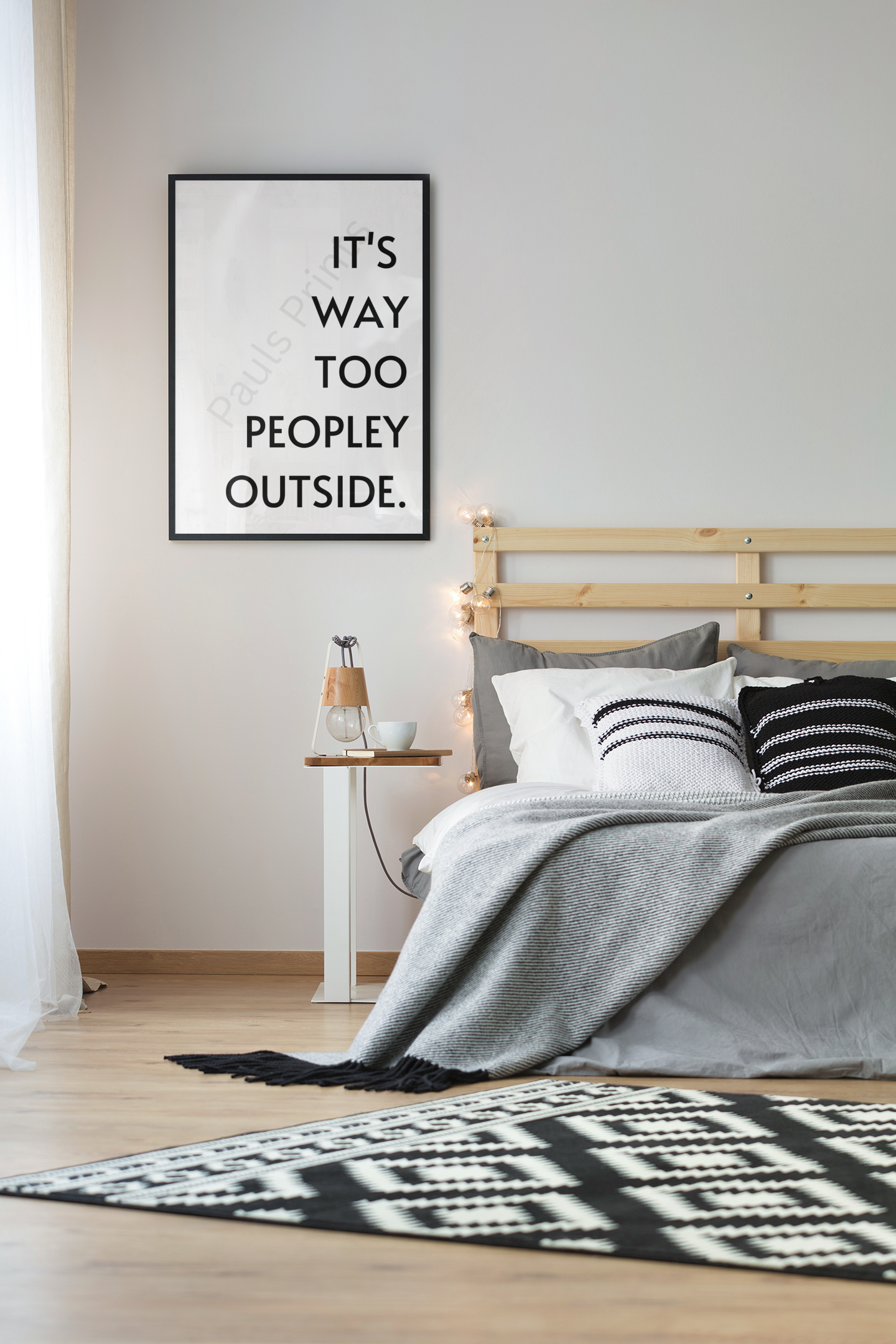 Framed black and white wall art with the quote “It’s Way Too Peopley Outside” hanging above a wooden bed with grey and white bedding.