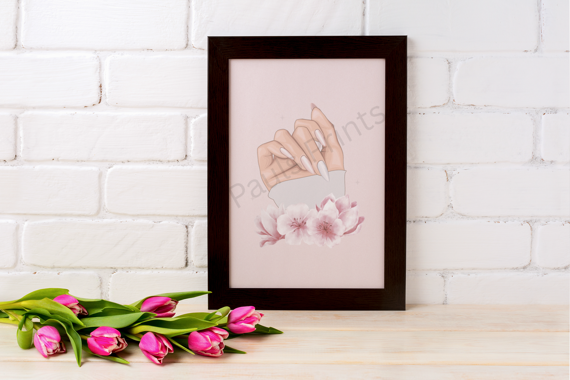 Framed illustration of a manicured hand surrounded by soft pink flowers, placed against a white brick wall with tulips.