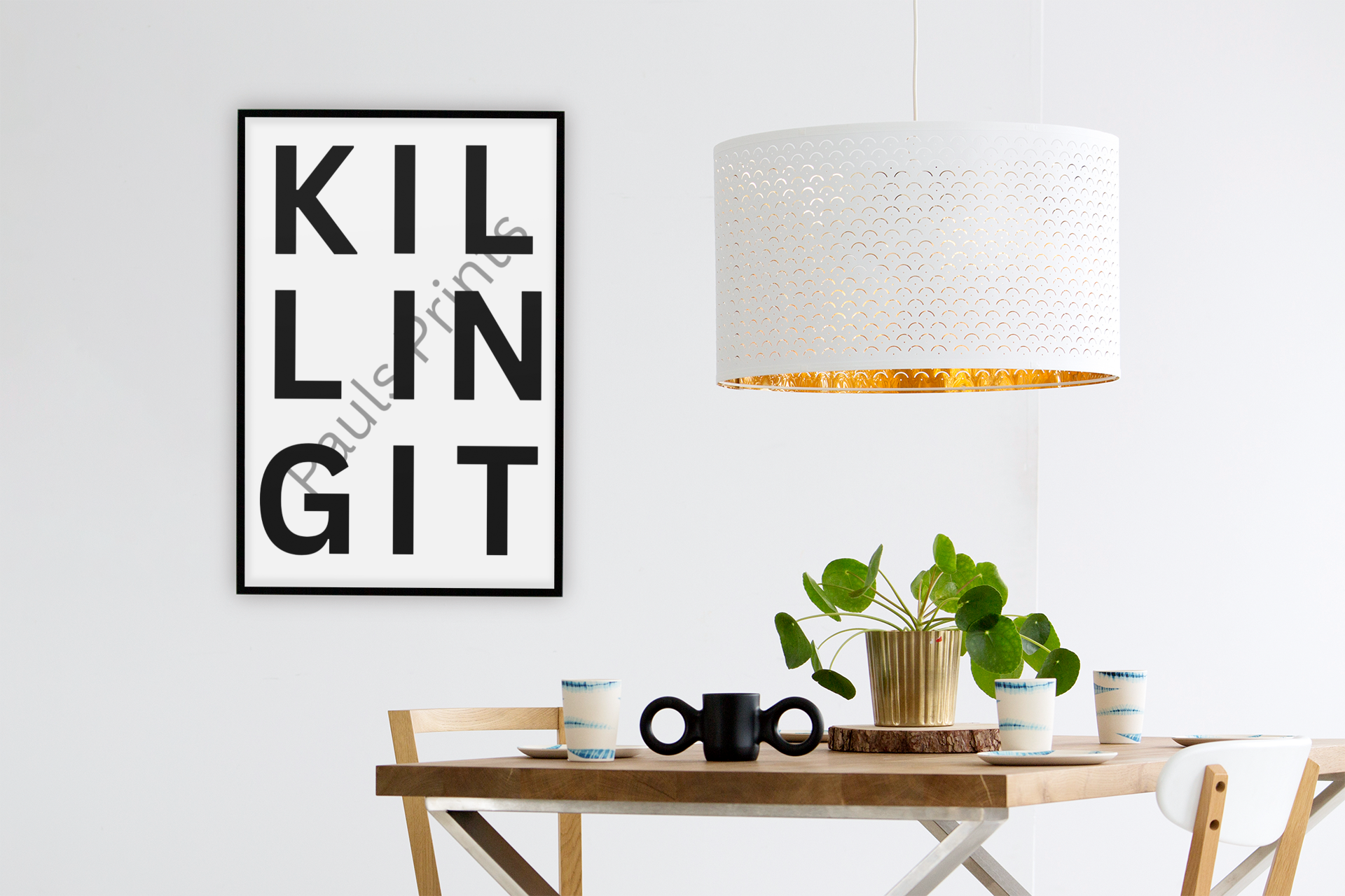 Bold black and white “Killing It” typography print hanging on a white wall above a modern dining table with wooden chairs and houseplants.