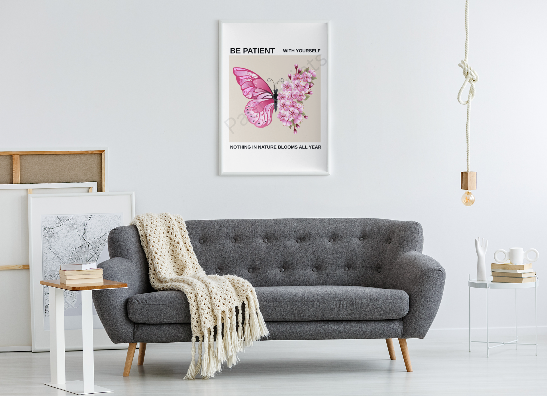 Framed pink butterfly and blossom inspirational print hanging above grey sofa in a bright, minimal living room with white walls and cosy décor.