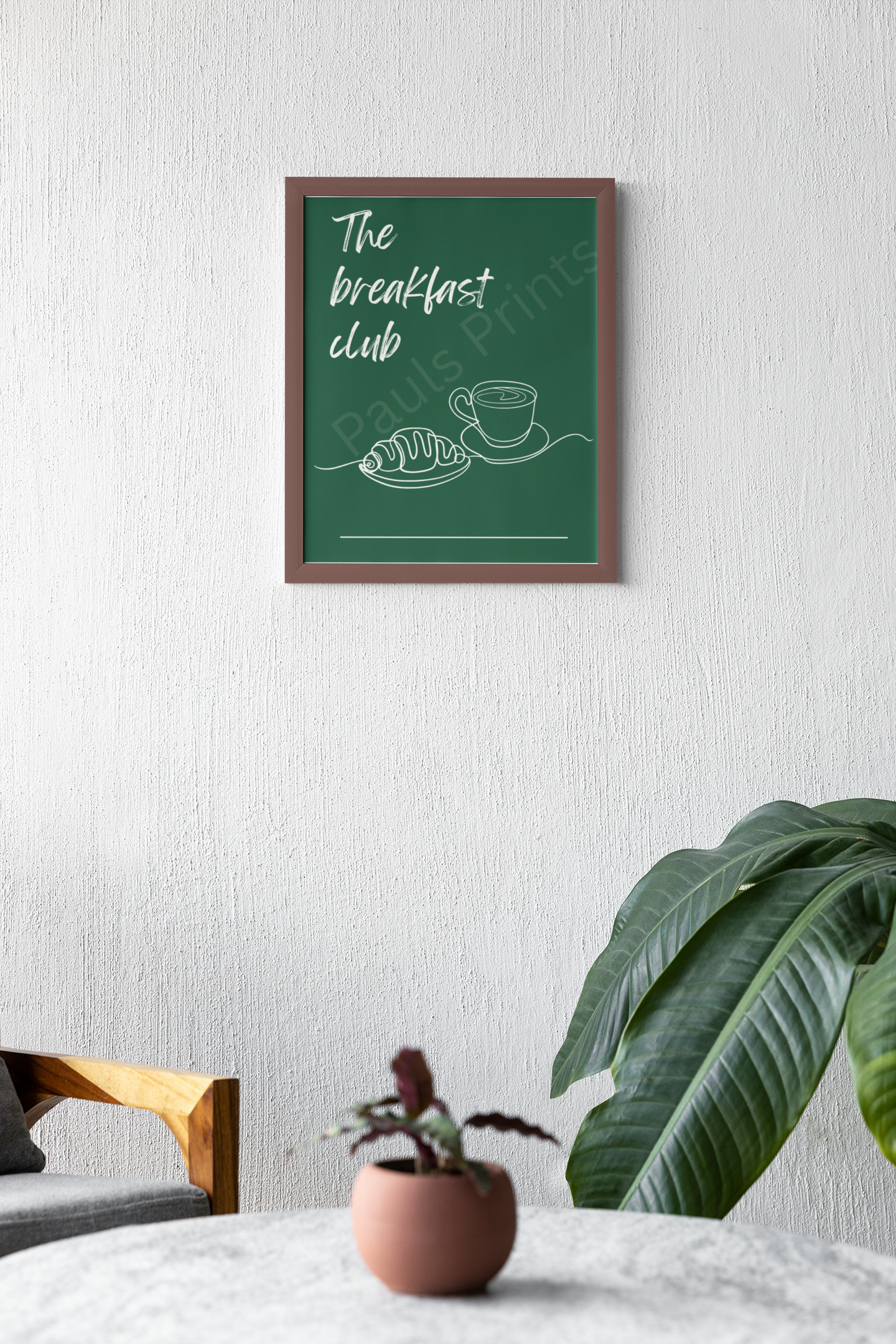 Clean white wall with framed "The Breakfast Club" artwork, accented by a soft green plant, pink pot, and grey coffee table in a relaxed seating area.