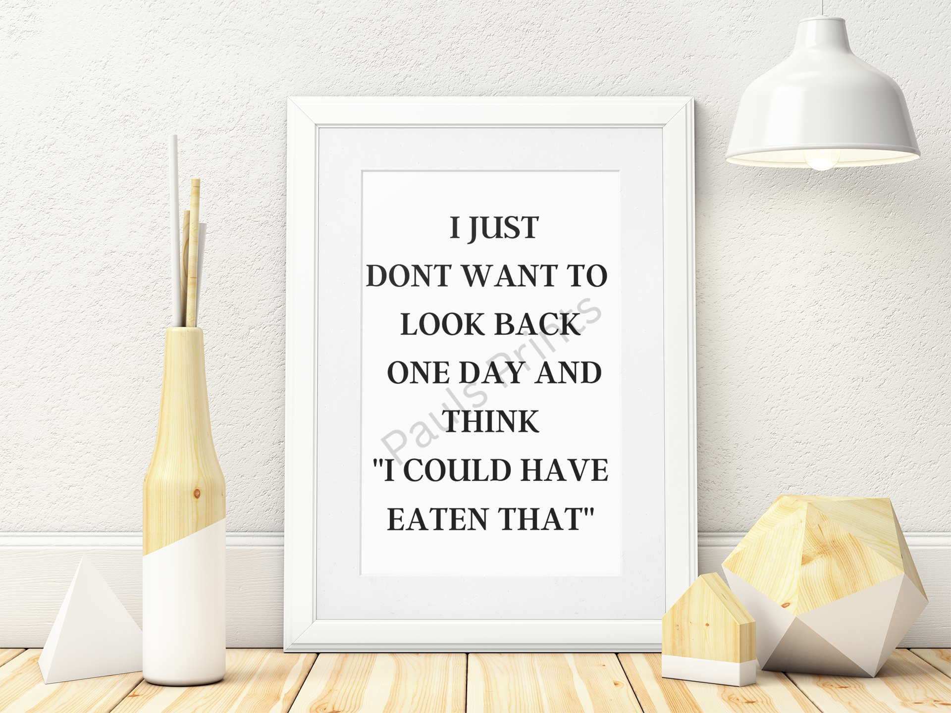 White-framed print with the quote “I just don’t want to look back one day and think I could have eaten that” displayed on a light wooden floor with decorative objects.