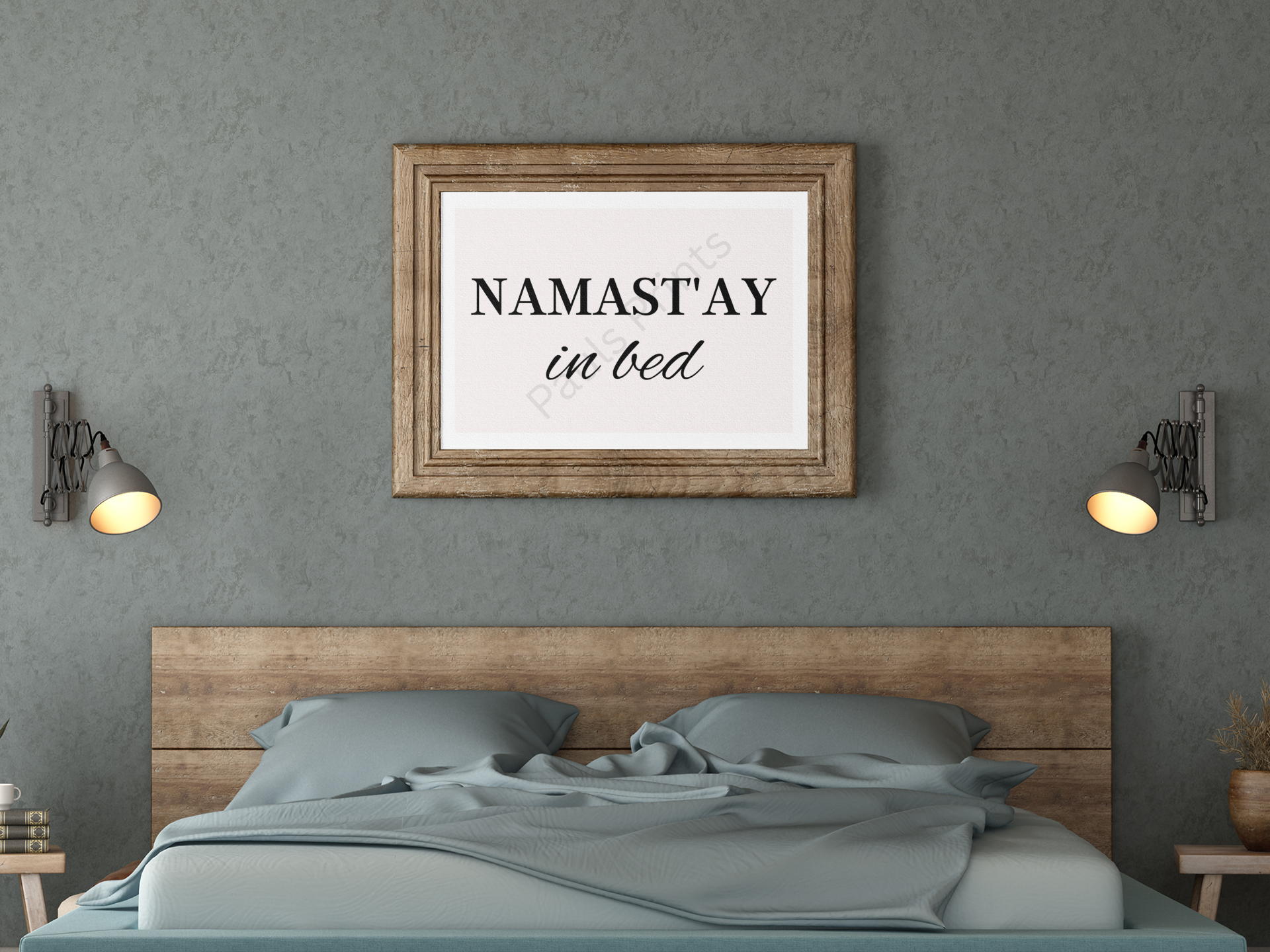 Framed “Namast’ay in Bed” print above a wooden bed with teal bedding and matching wall lamps.