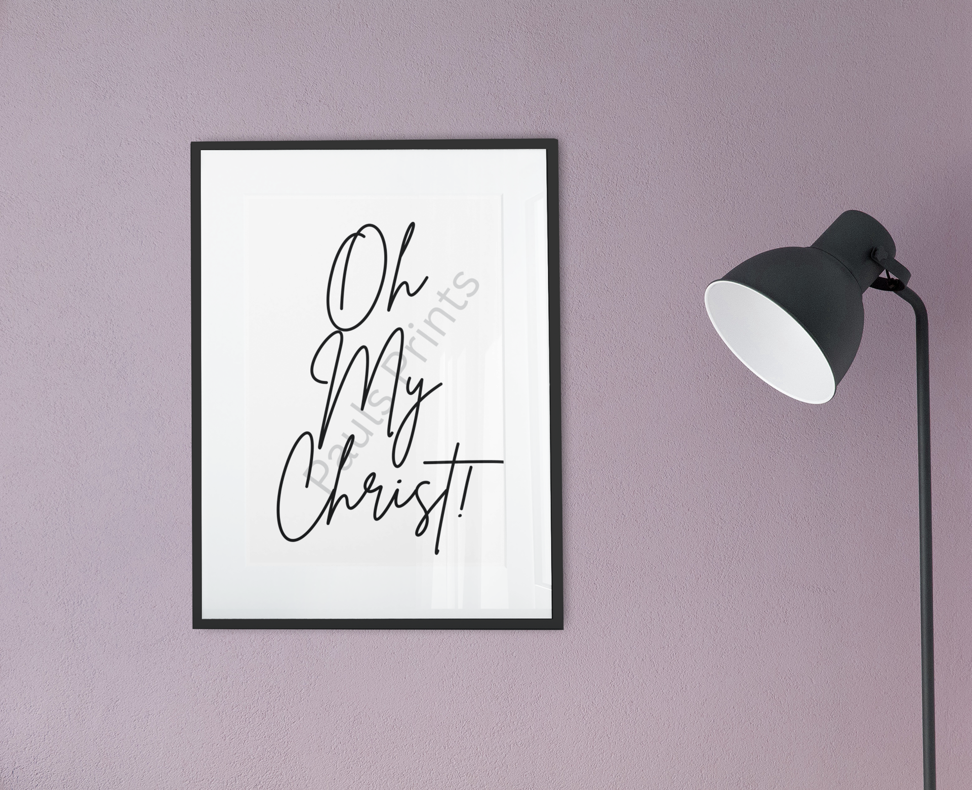 Black framed Oh My Christ print with cursive lettering, mounted on a mauve wall beside a modern black floor lamp.