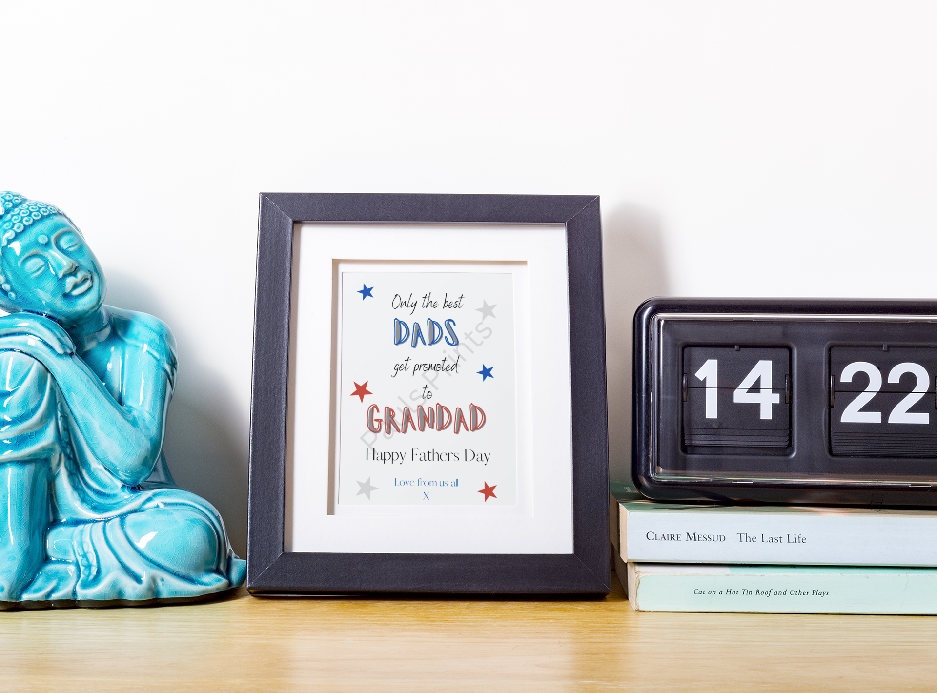 Framed Grandad print on white background with blue Buddha figurine, flip clock, and stacked books.