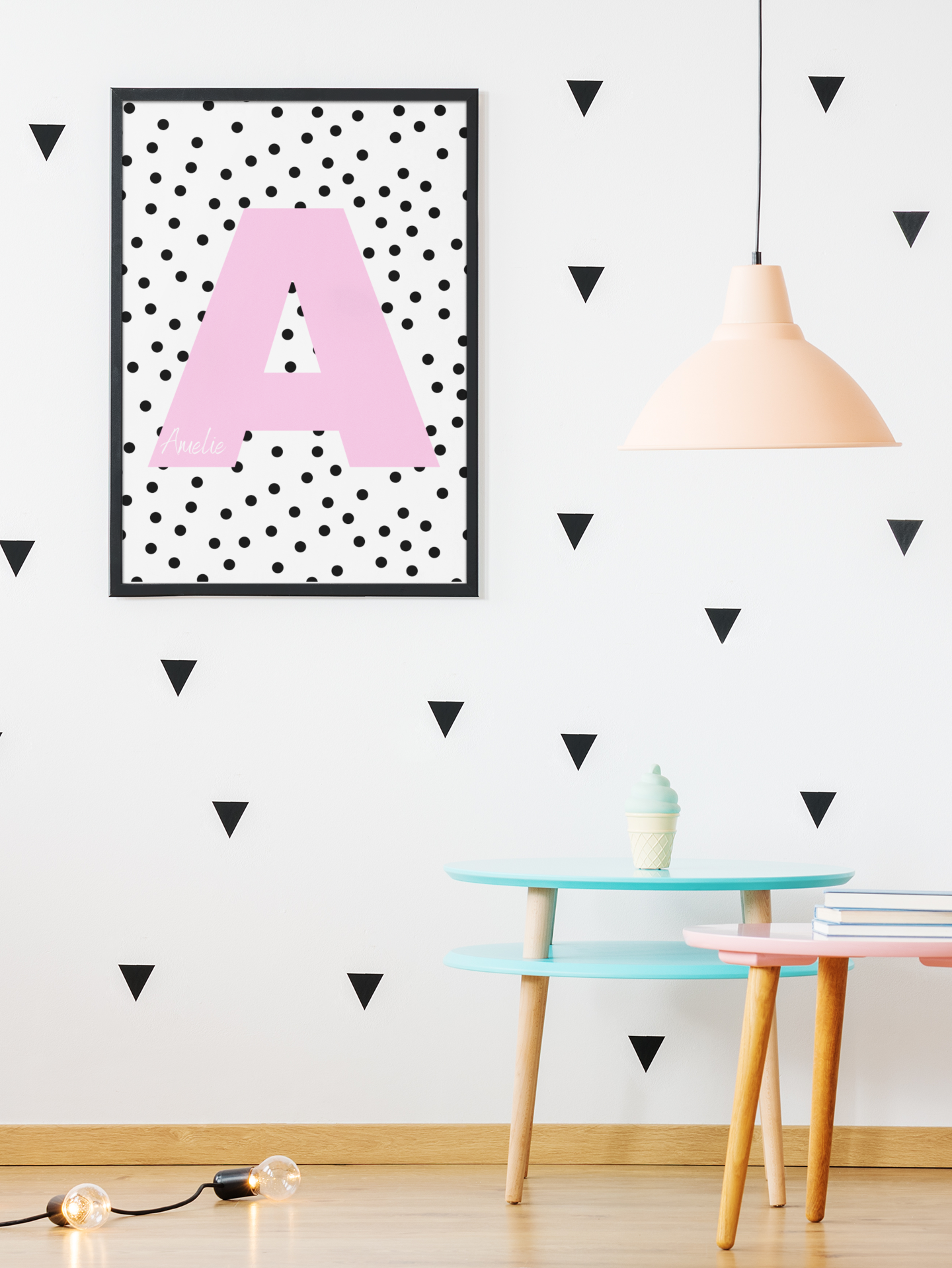 Framed print with pink letter A and black polka dots on a white background, styled in a playful child's room with triangle wall decals.