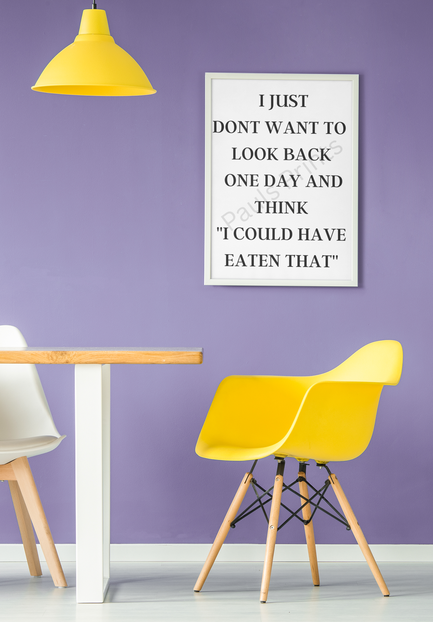 Framed print with the quote “I just don’t want to look back one day and think I could have eaten that” on a purple wall above a yellow chair and dining table.