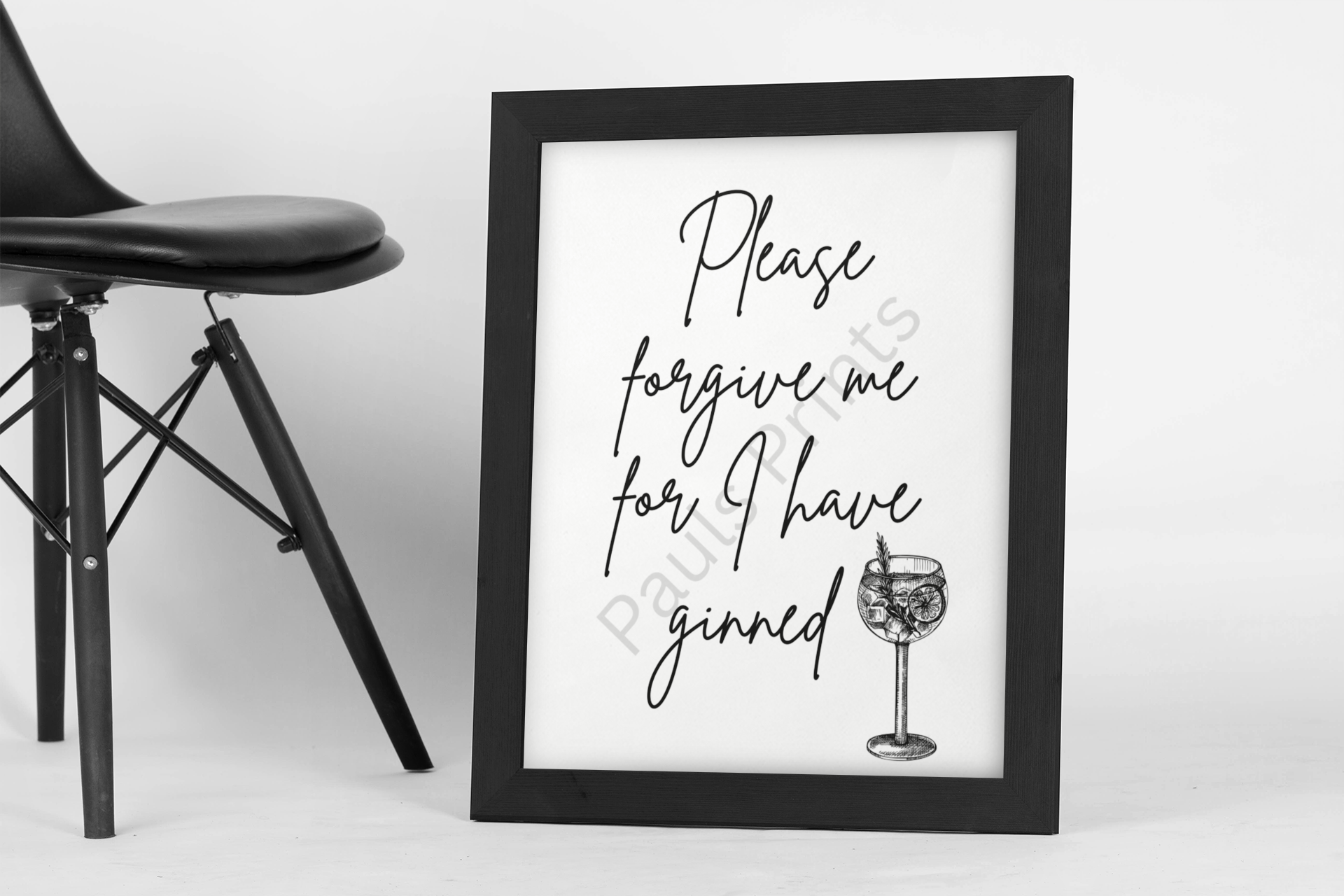 Minimalist gin pun wall art in a black frame leaning against wall beside black chair.