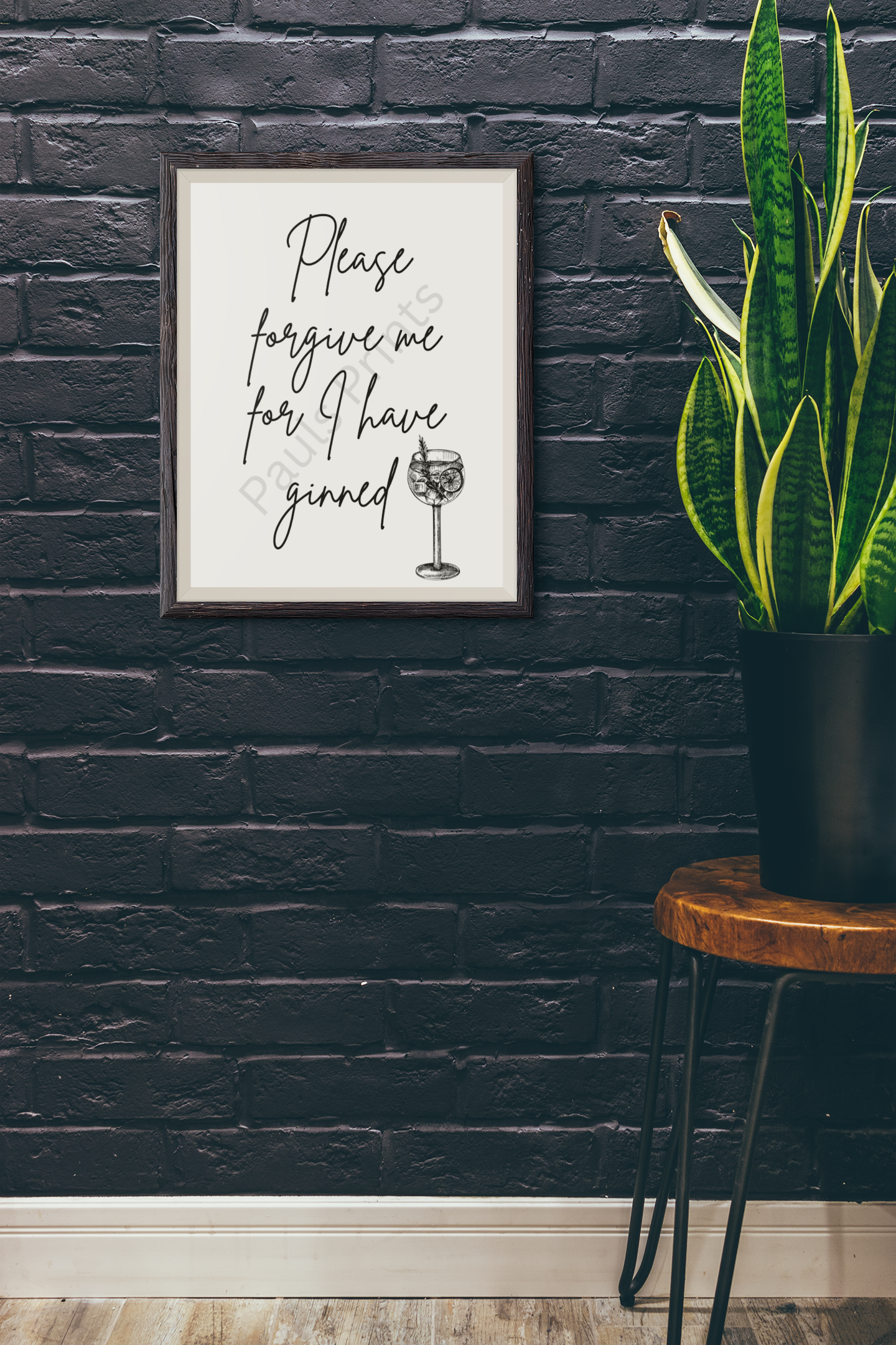 Humorous gin wall art in rustic wood frame mounted on black brick wall beside potted plant.