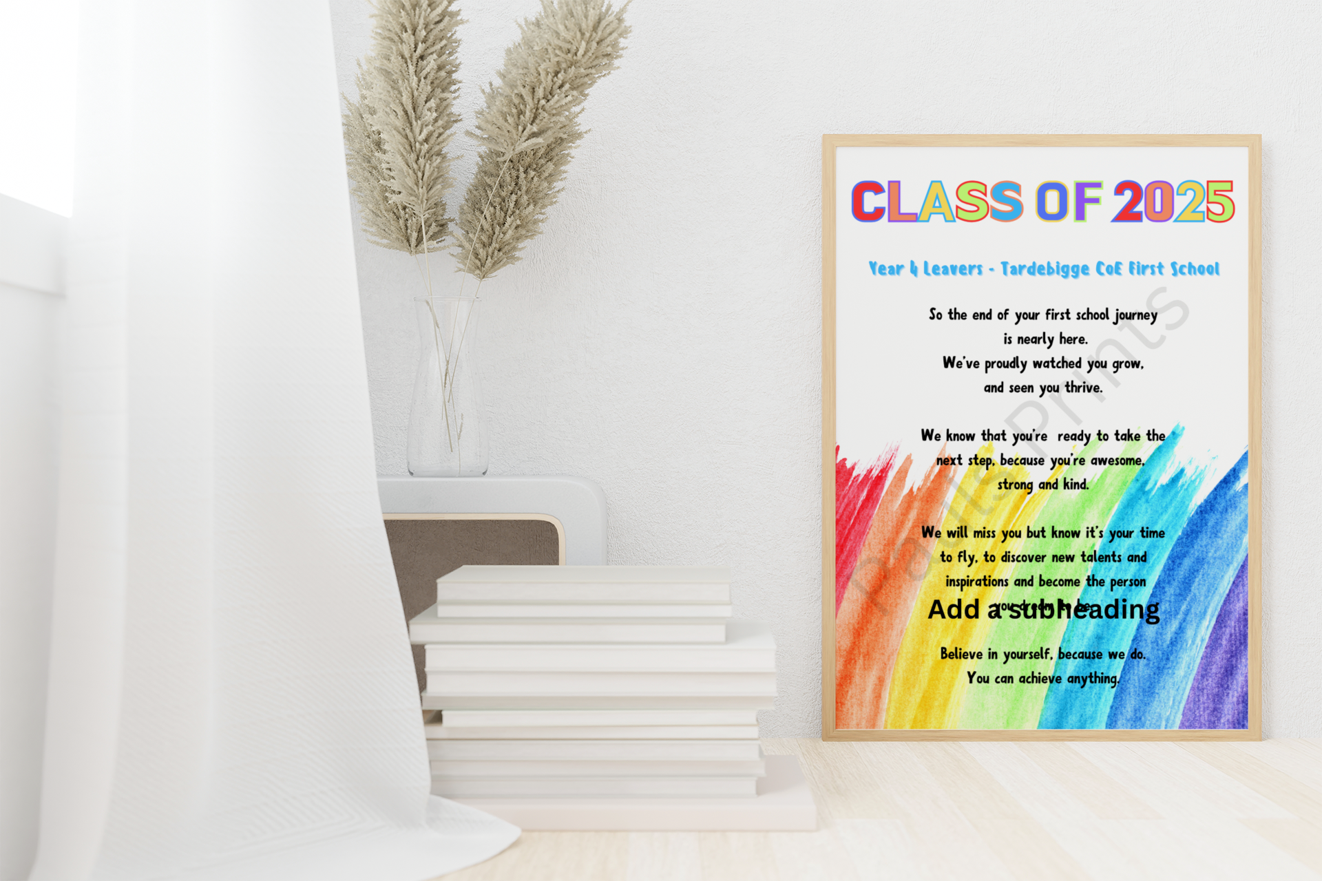 “Class of 2025” rainbow leavers poem in a light wooden frame, placed on the floor beside books and a vase with pampas grass.